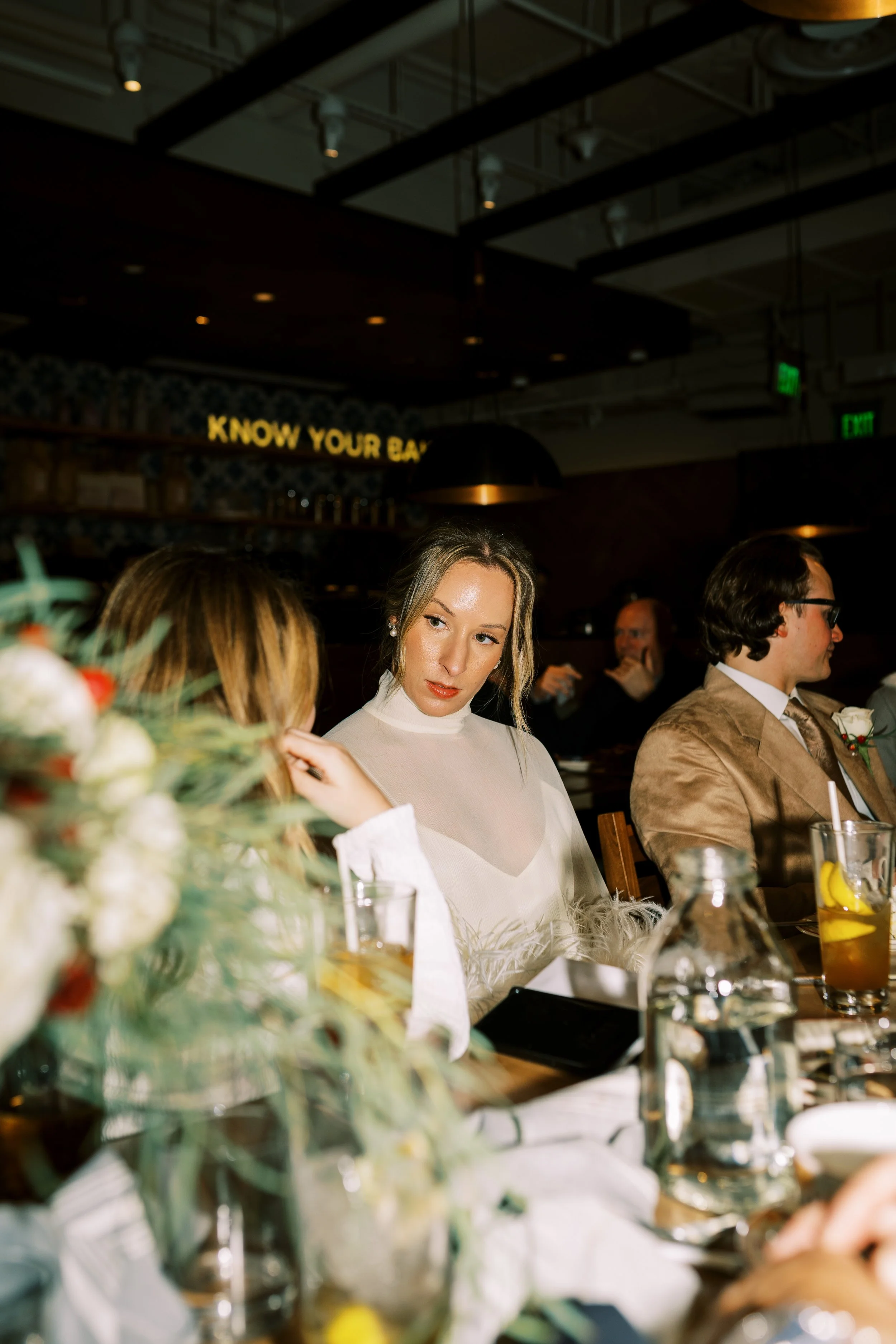 Bride and groom seated together at a restaurant table with wine glasses and greenery decor