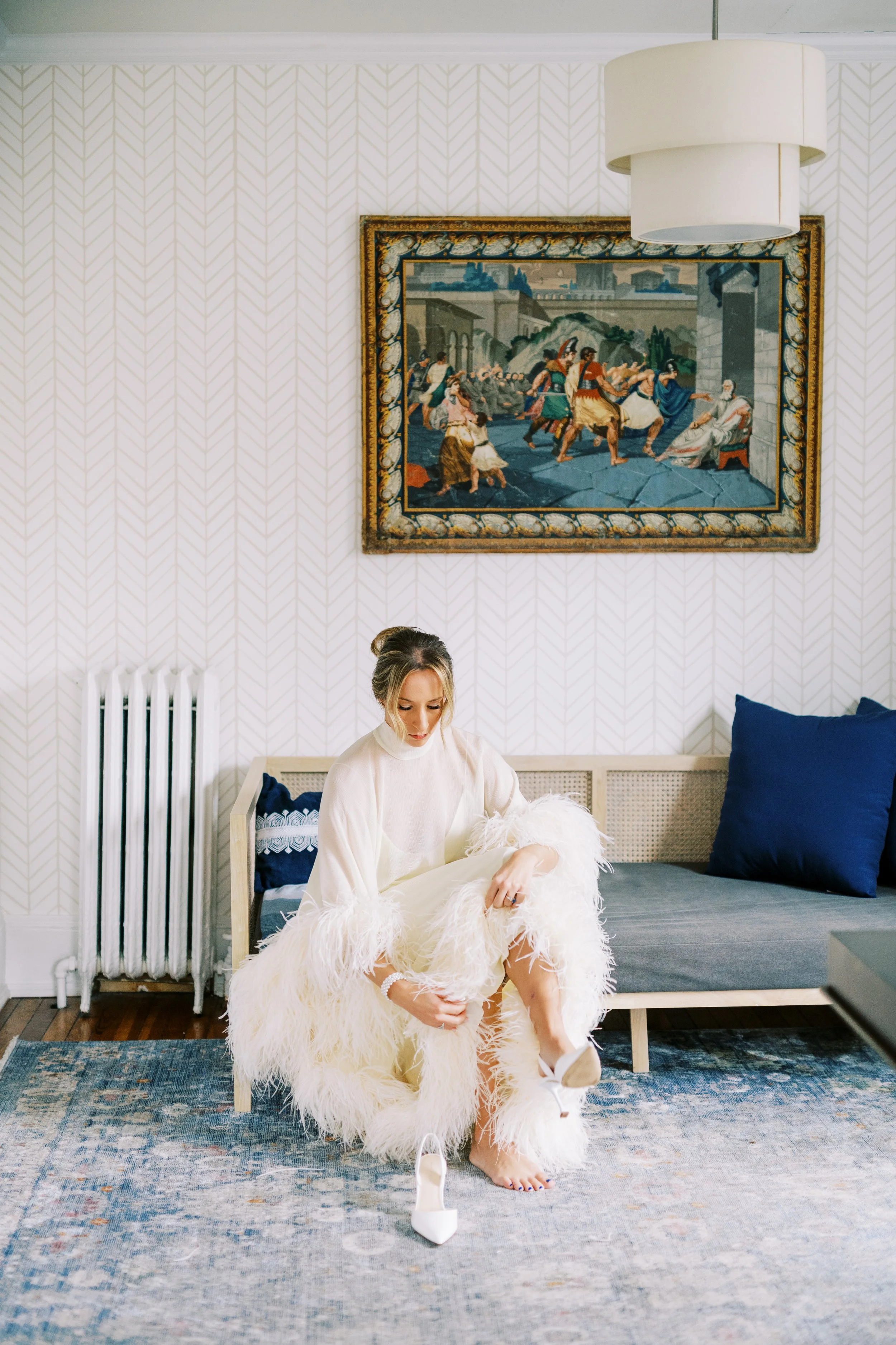 Bride seated in an elegant living room getting ready, framed art on the wall behind her