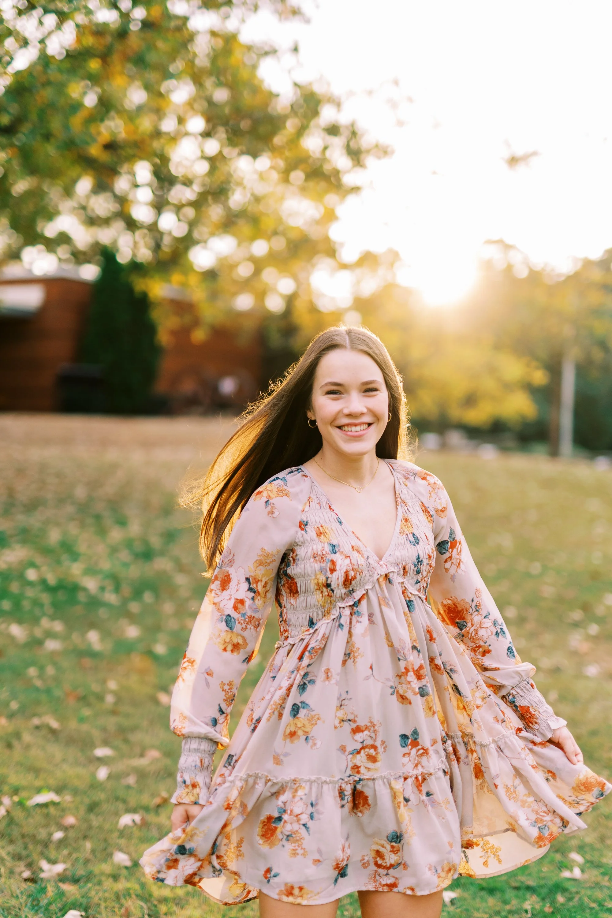 Senior portrait of Hannah smiling brightly in a floral dress on a sunlit lawn at Kennesaw Mountain Battlefield Park in Kennesaw, Georgia