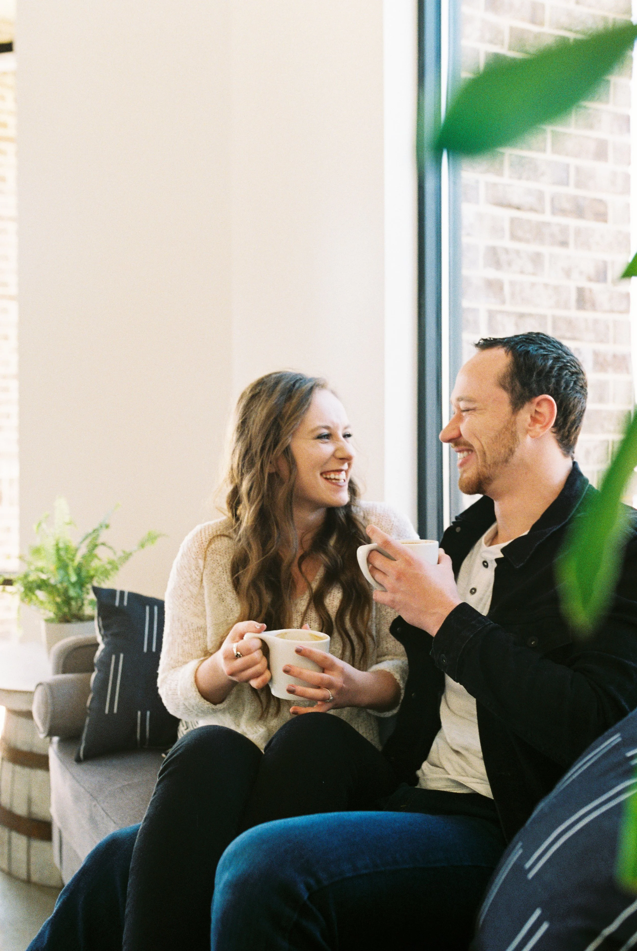 Conner and Maddie laugh together over coffee on a window-side couch in a Dallas, Georgia coffee shop.