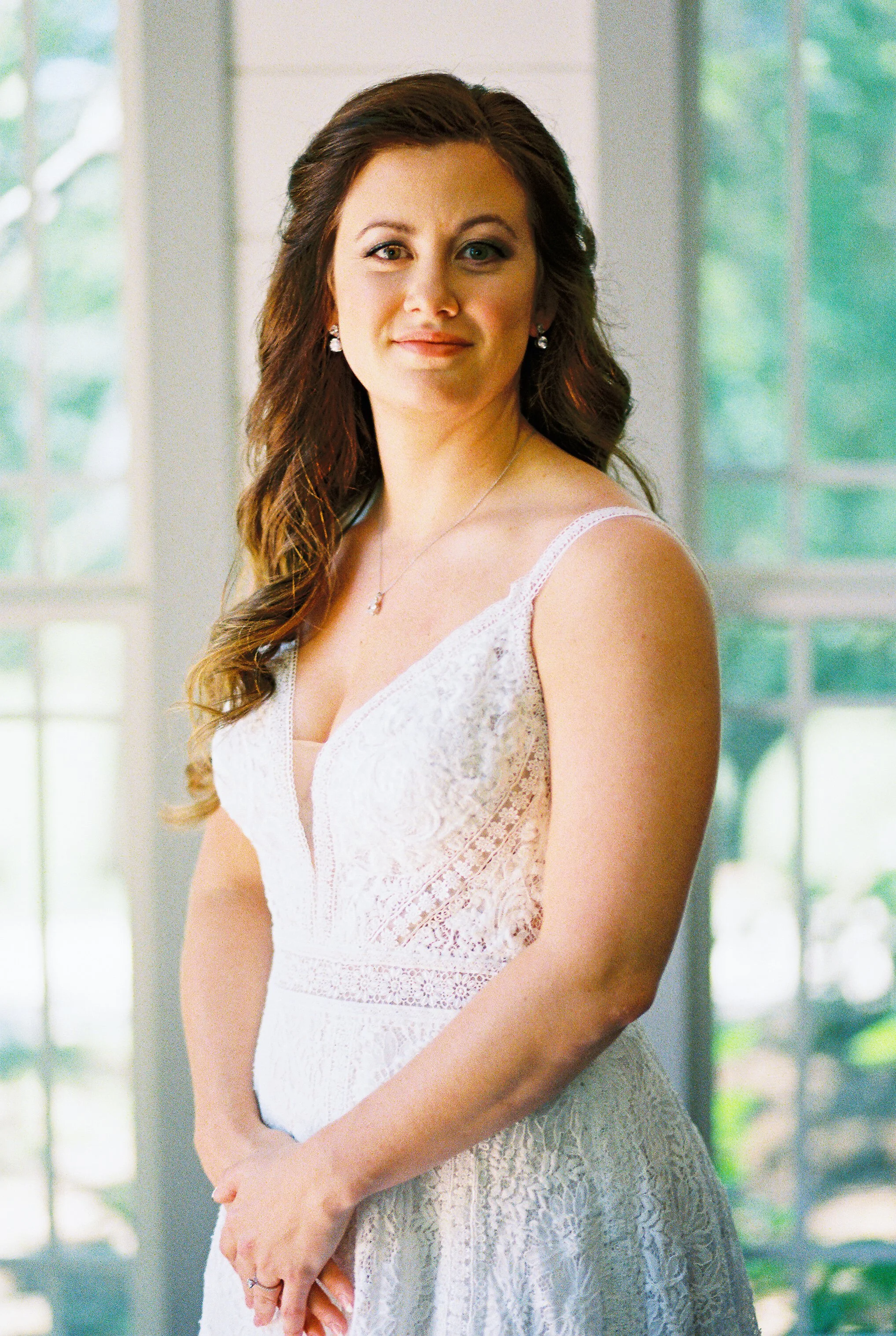 Bride standing indoors by a window, soft natural light, hands clasped calmly