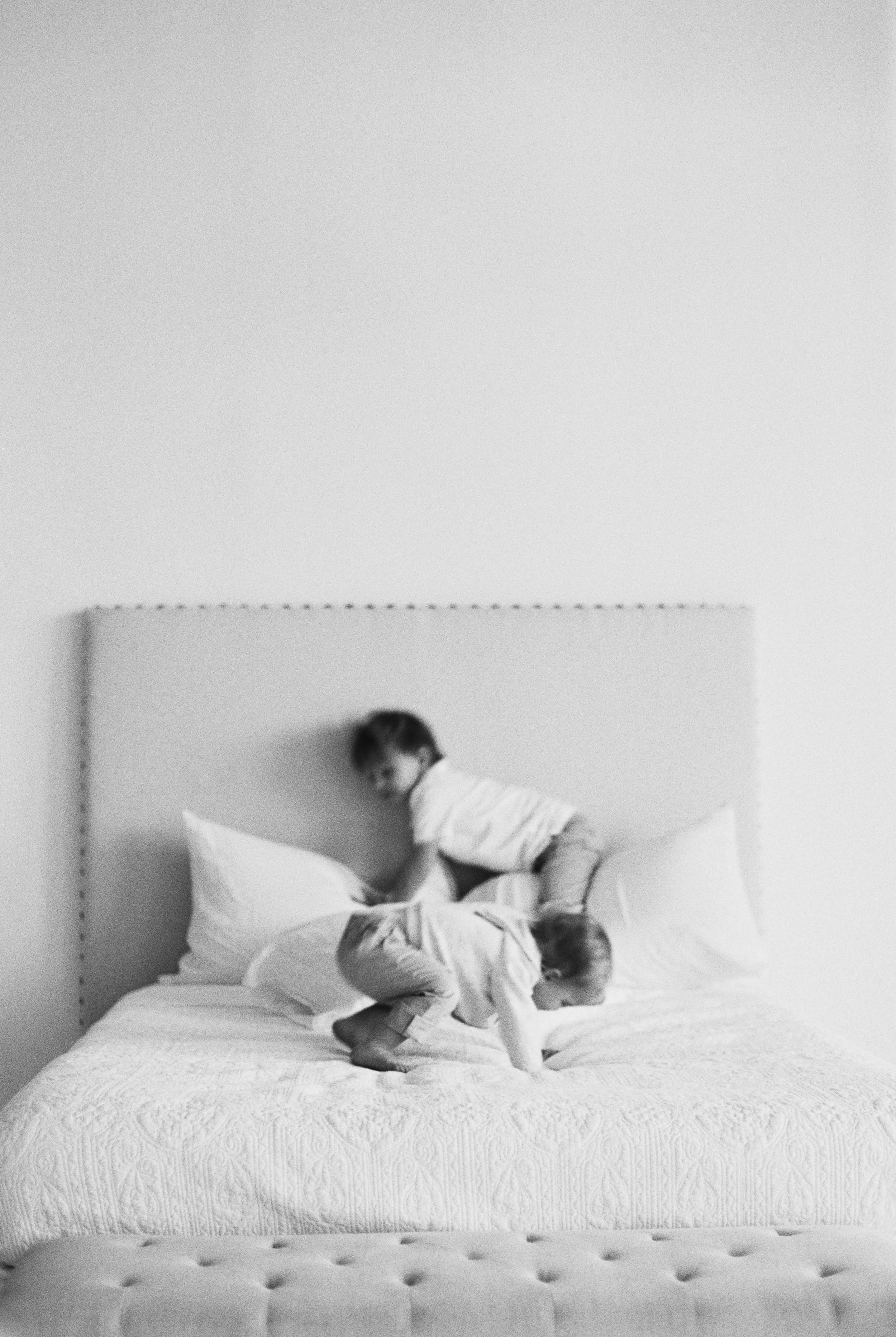 Two young children playing on a bed with a headboard in a minimalistic room.