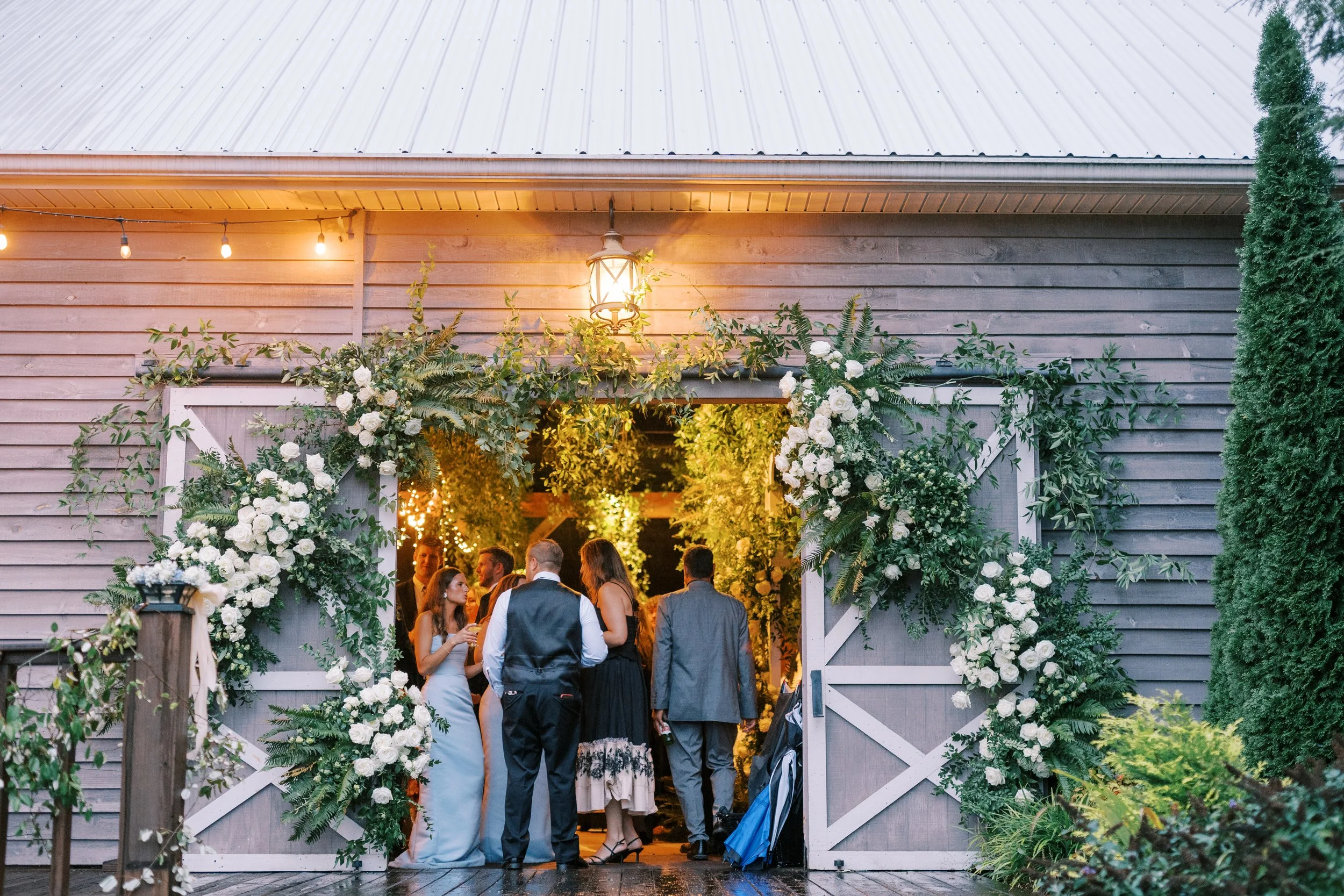 Guests entering reception barn doorway framed with greenery and string lights