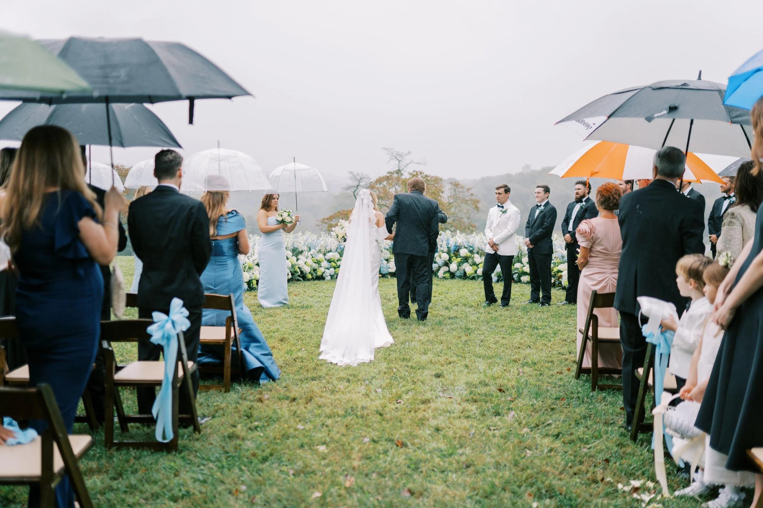 Bridal processional with guests holding colorful umbrellas along the aisle