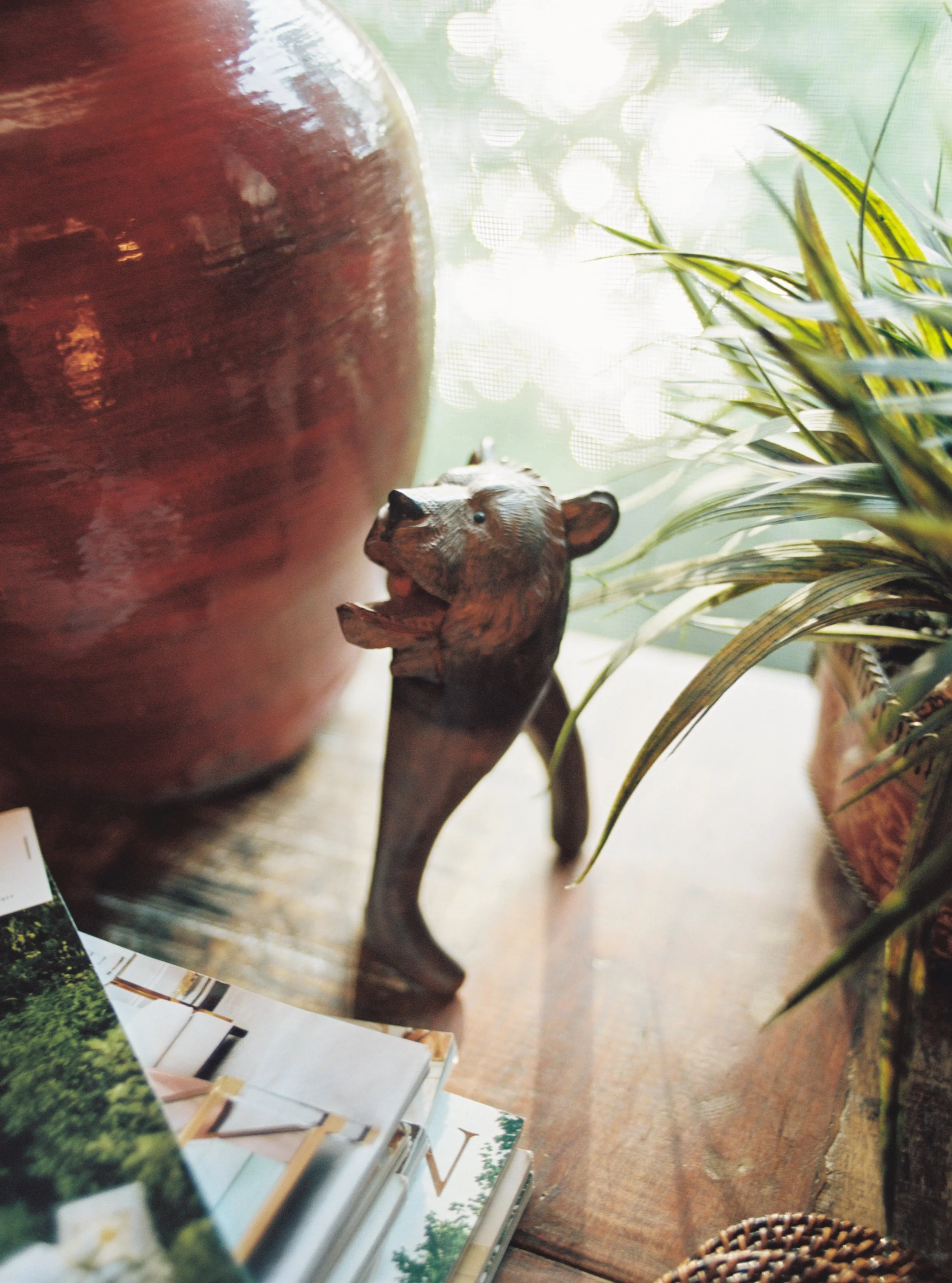 Carved wooden bear figurine displayed with a red ceramic vase and greenery, interior decor detail
