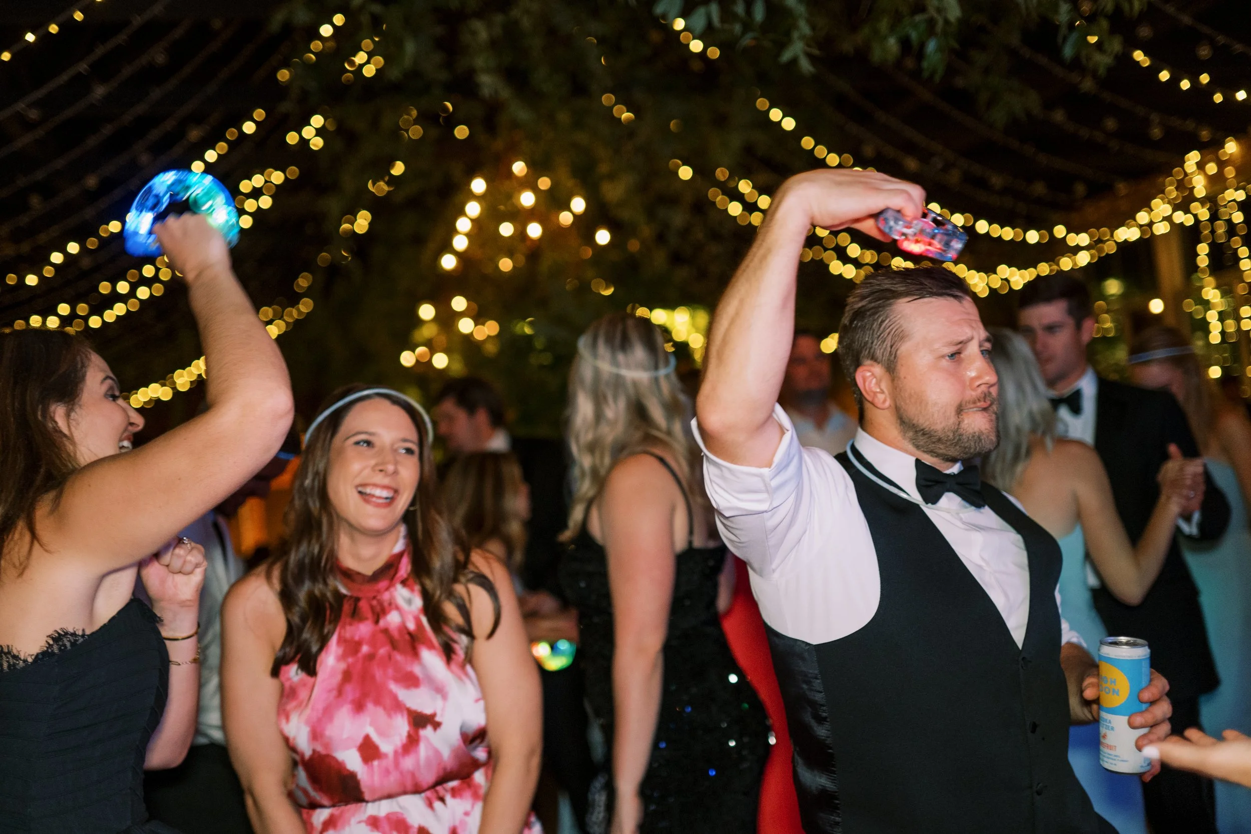Guests dancing with glow sticks under string lights at the reception