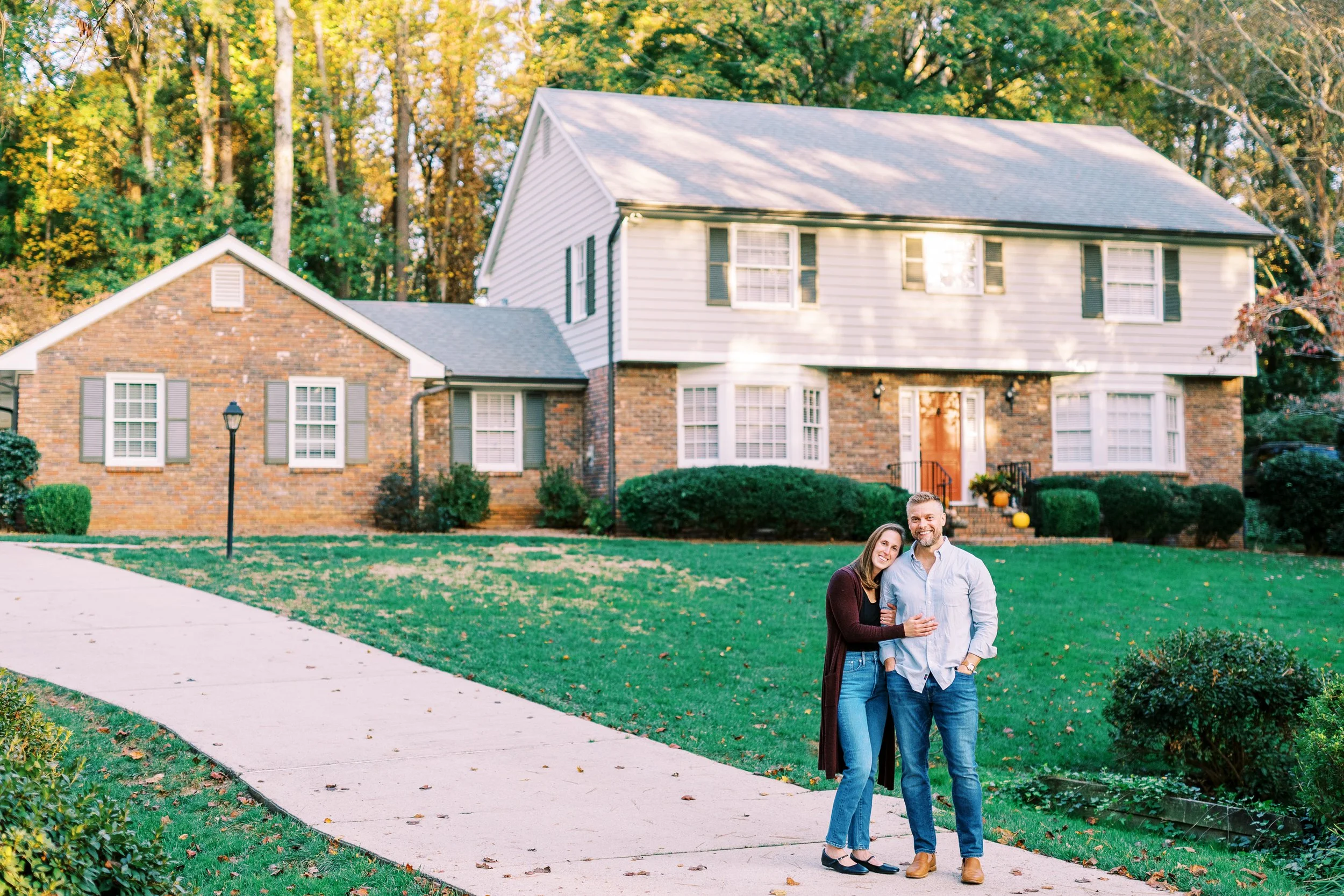 Holly and Chris standing together in the driveway in front of their brick colonial home in Dunwoody, Georgia