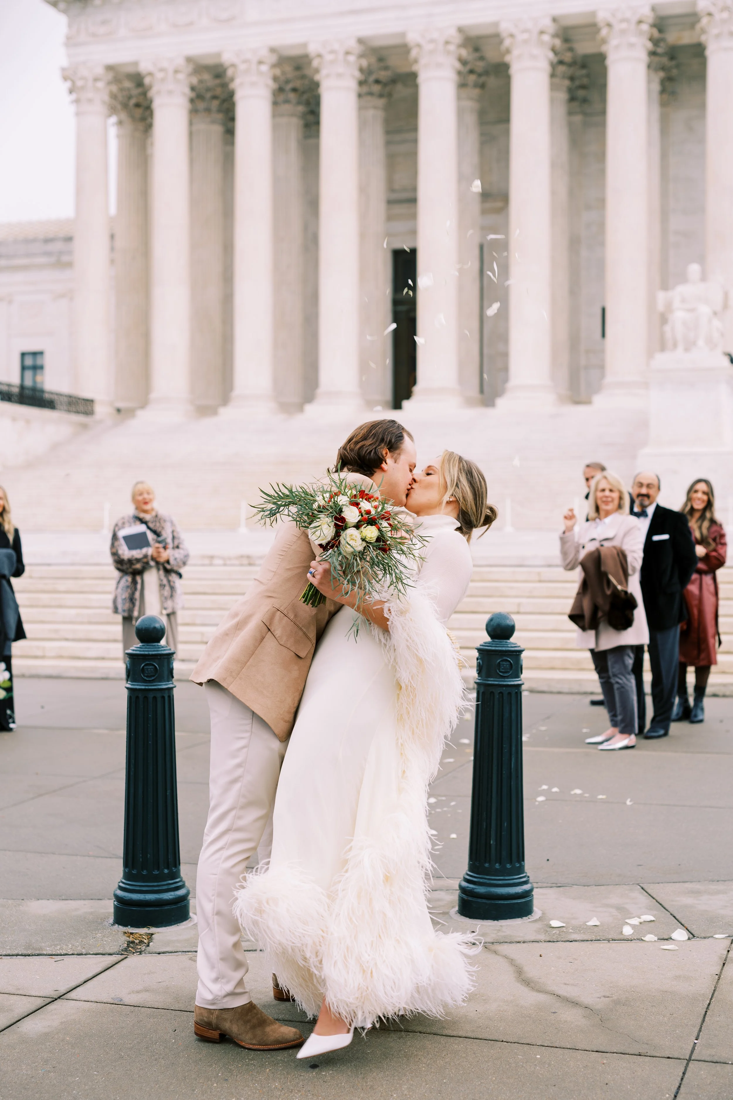 Bride and groom kissing on the steps of a grand columned building in Washington DC surrounded by guests