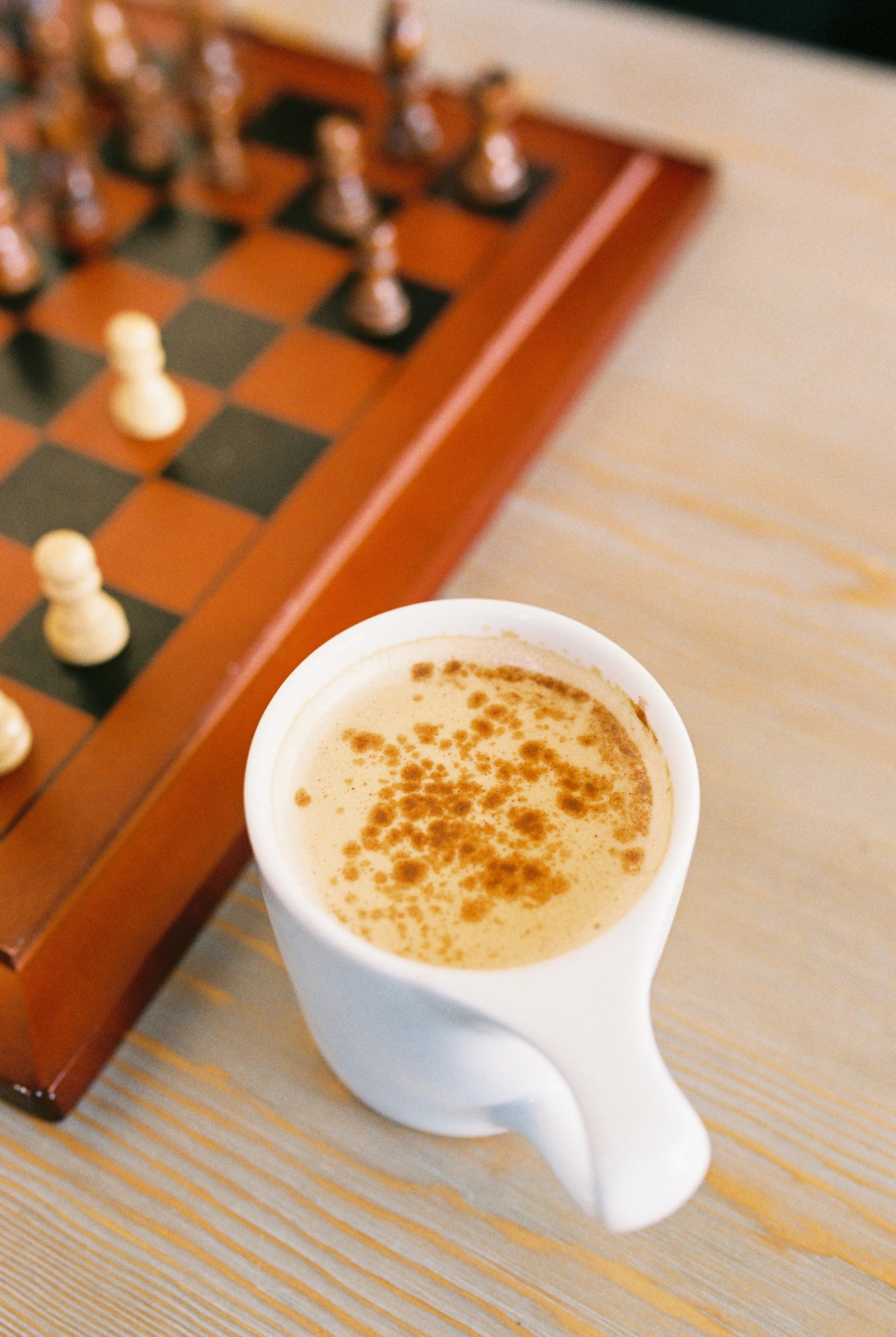 A still life of a latte with latte art beside a wooden chess board in a Dallas, Georgia coffee shop.