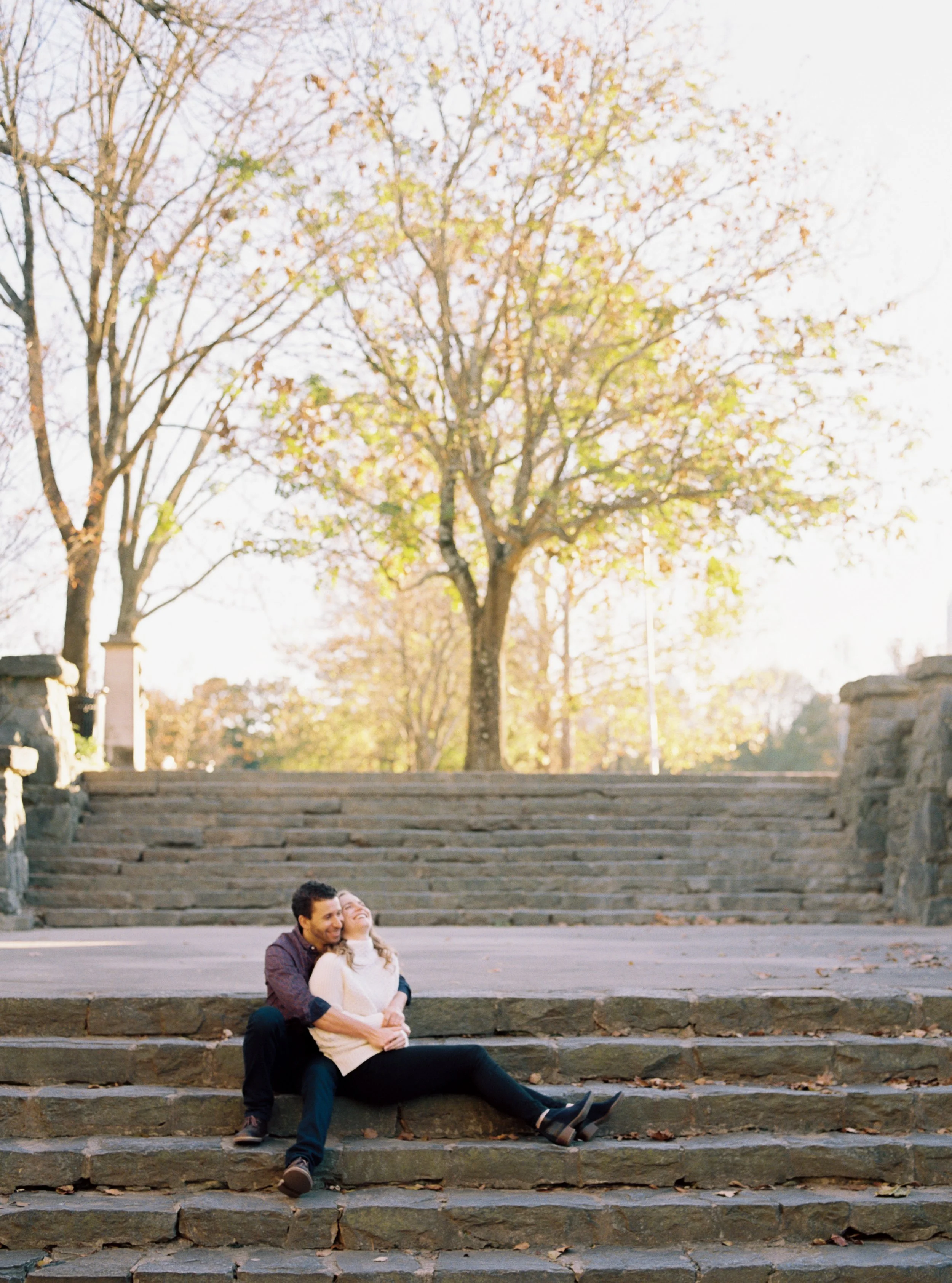 Couple sitting together on wide stone amphitheater steps beneath an autumn tree