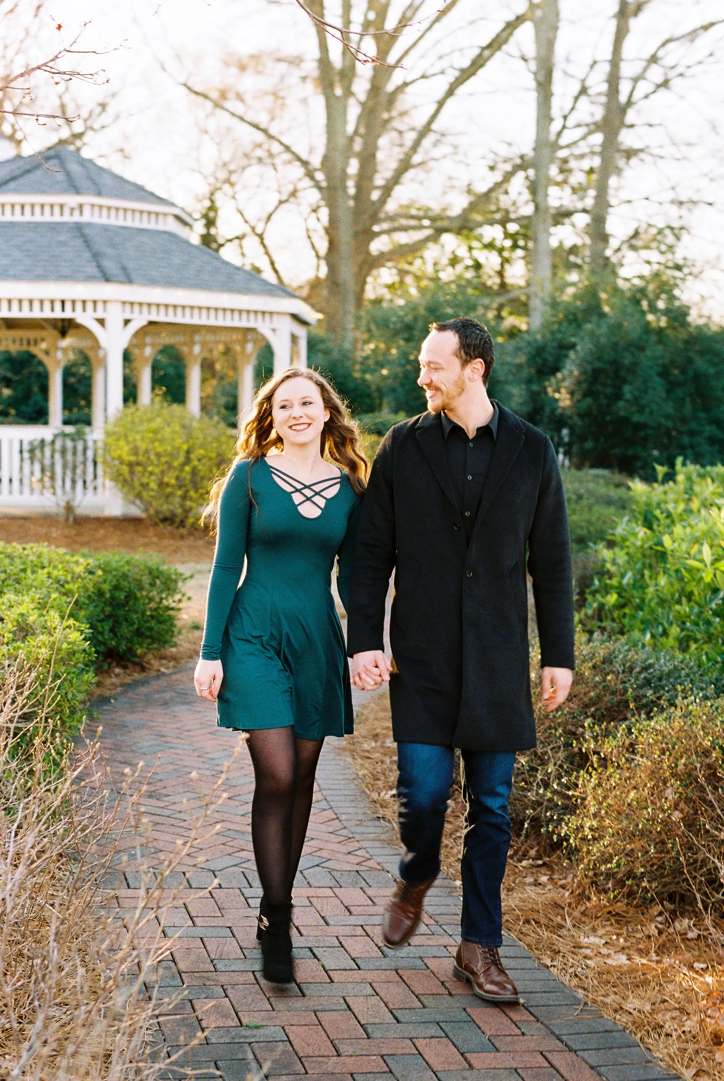 Conner and Maddie walk hand in hand toward the camera on a brick path near the gazebo in Dallas, Georgia.