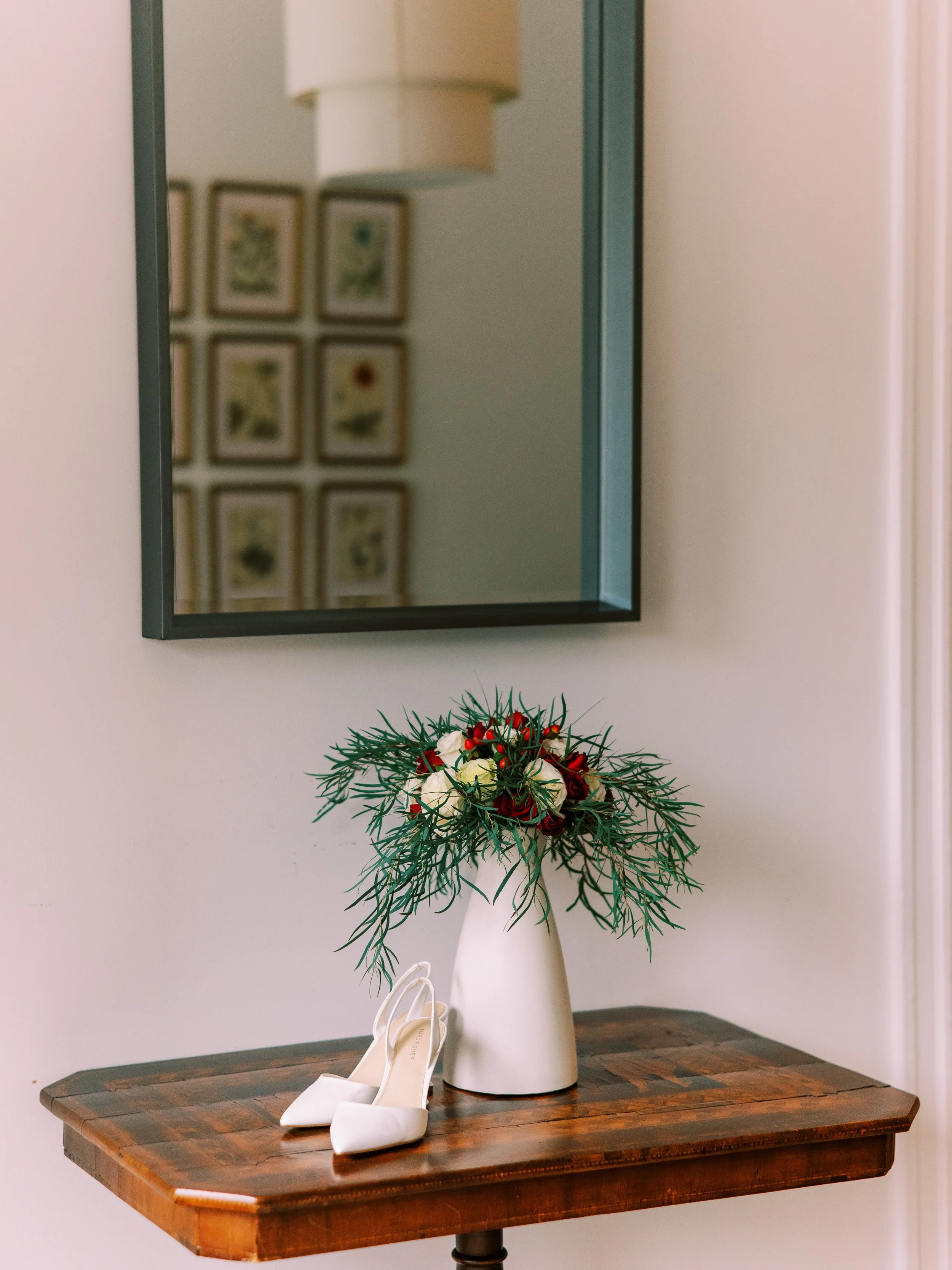 Floral arrangement and bridal shoes displayed on a table beneath a framed mirror at the restaurant