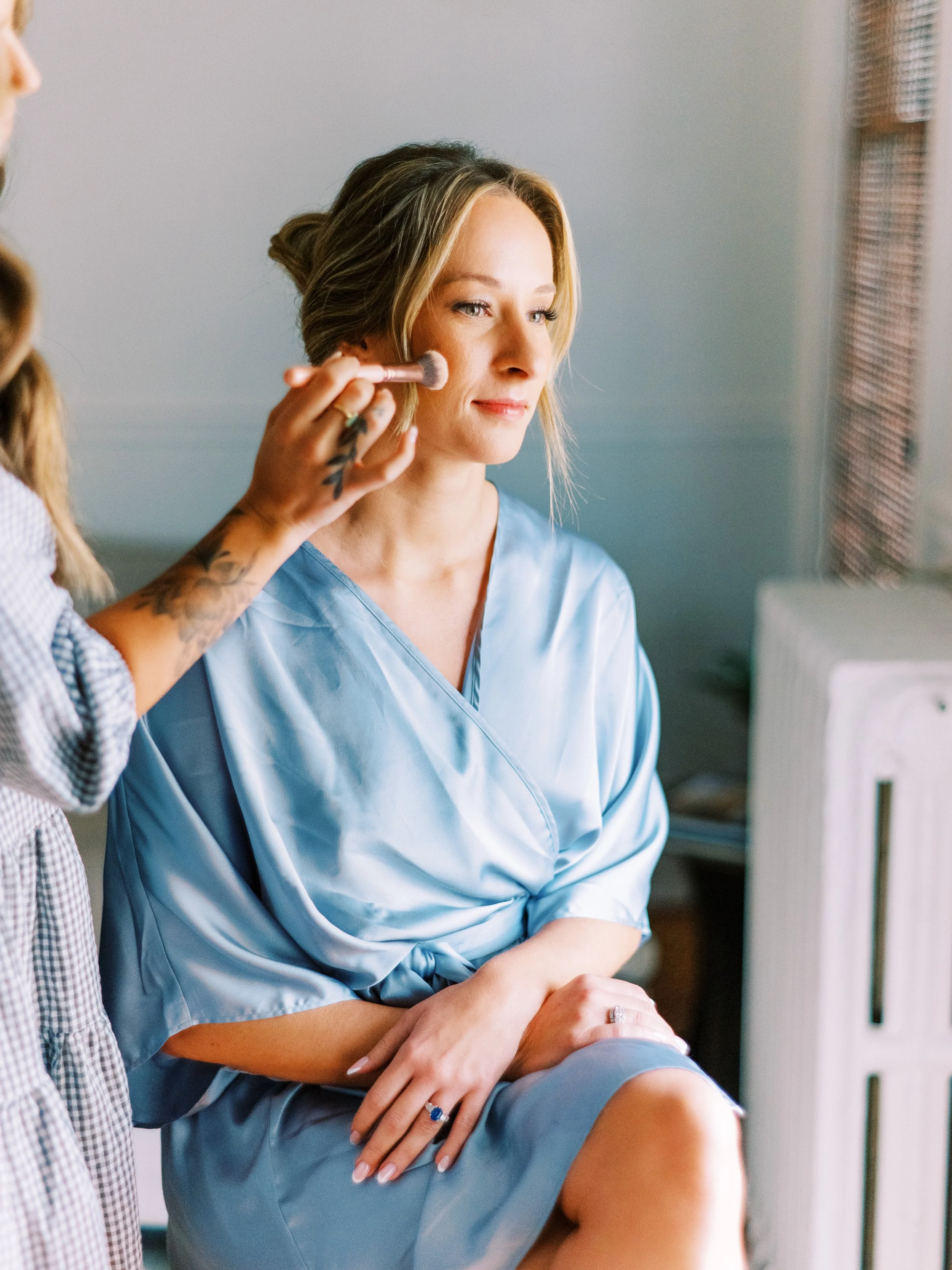 Bride applying makeup in a blue robe while getting ready