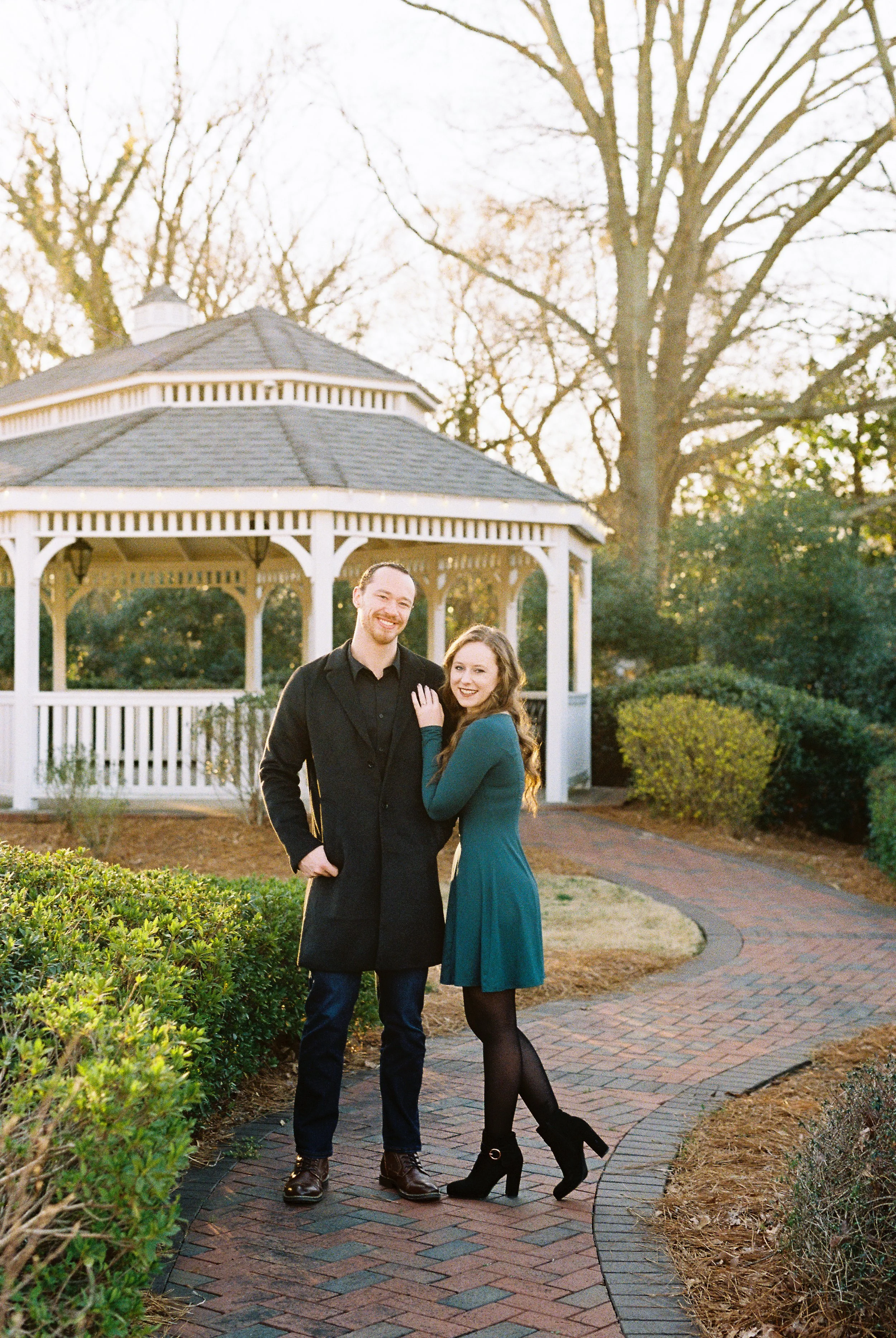 Conner and Maddie stand together on a brick path in front of a white gazebo at golden hour in Dallas, Georgia.