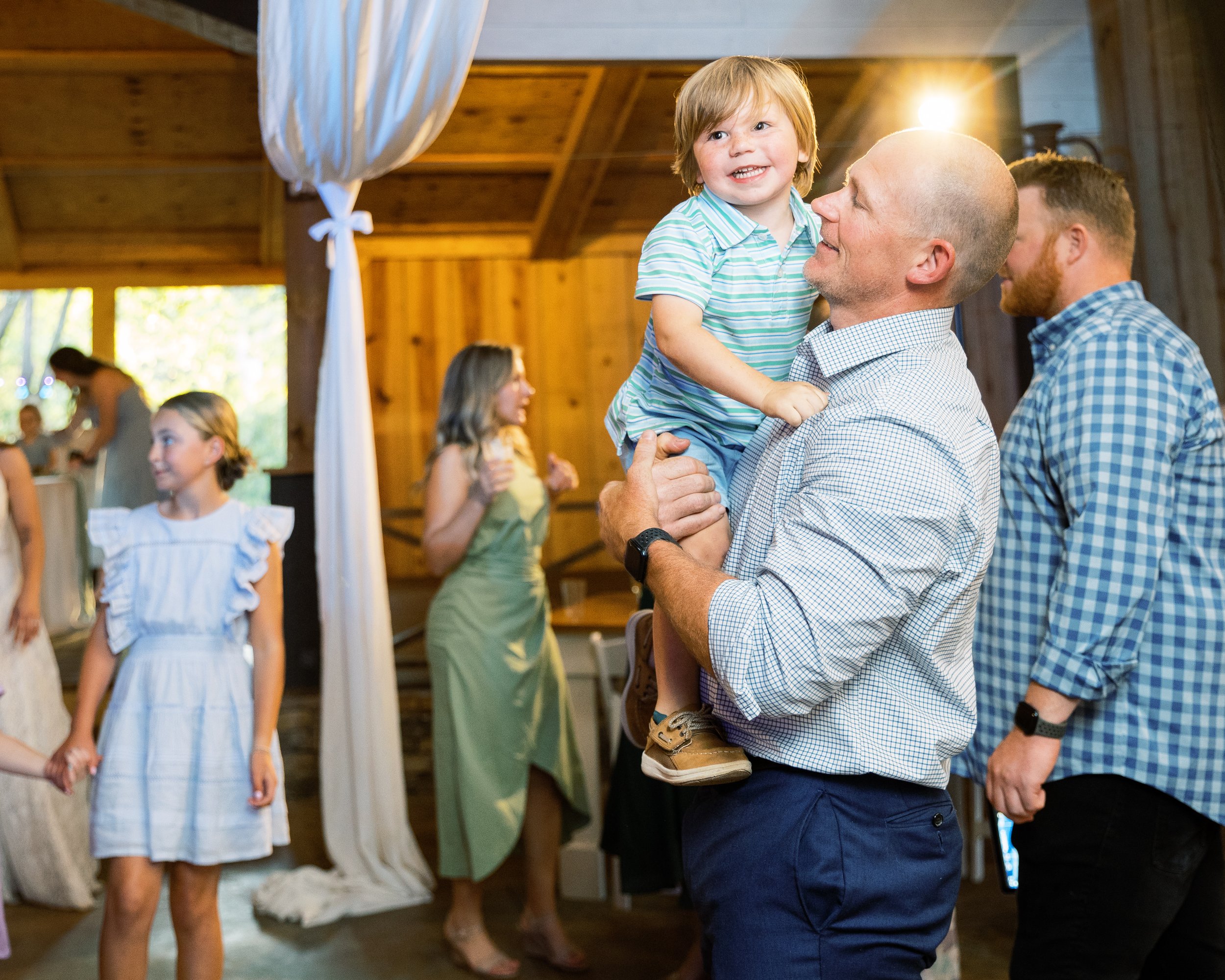 Guest holding up a young child while celebrating with others at the reception