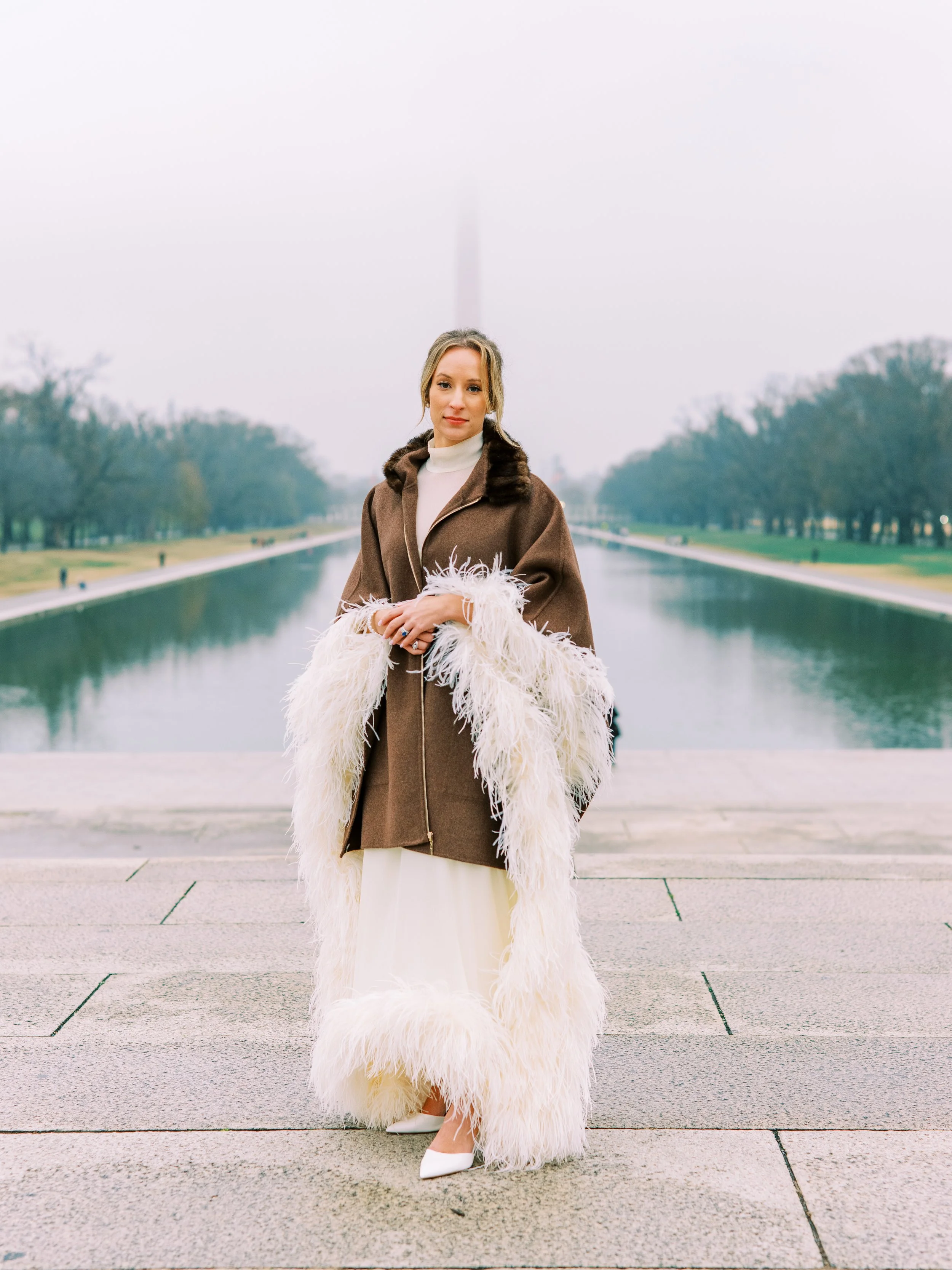 Bride standing solo in her fur coat beside the reflecting pool