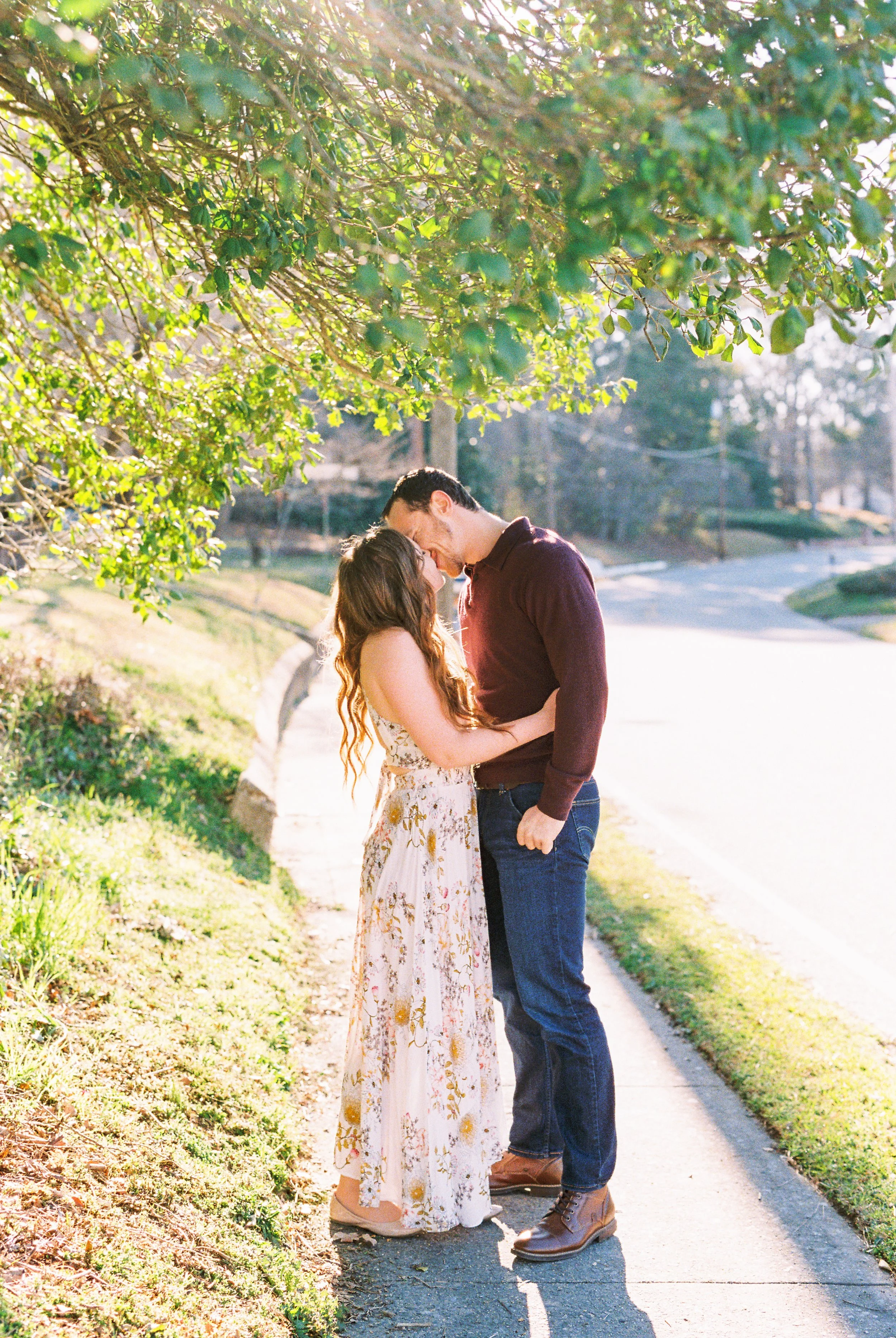 Conner and Maddie embrace beneath tree branches beside a path in Dallas, Georgia.