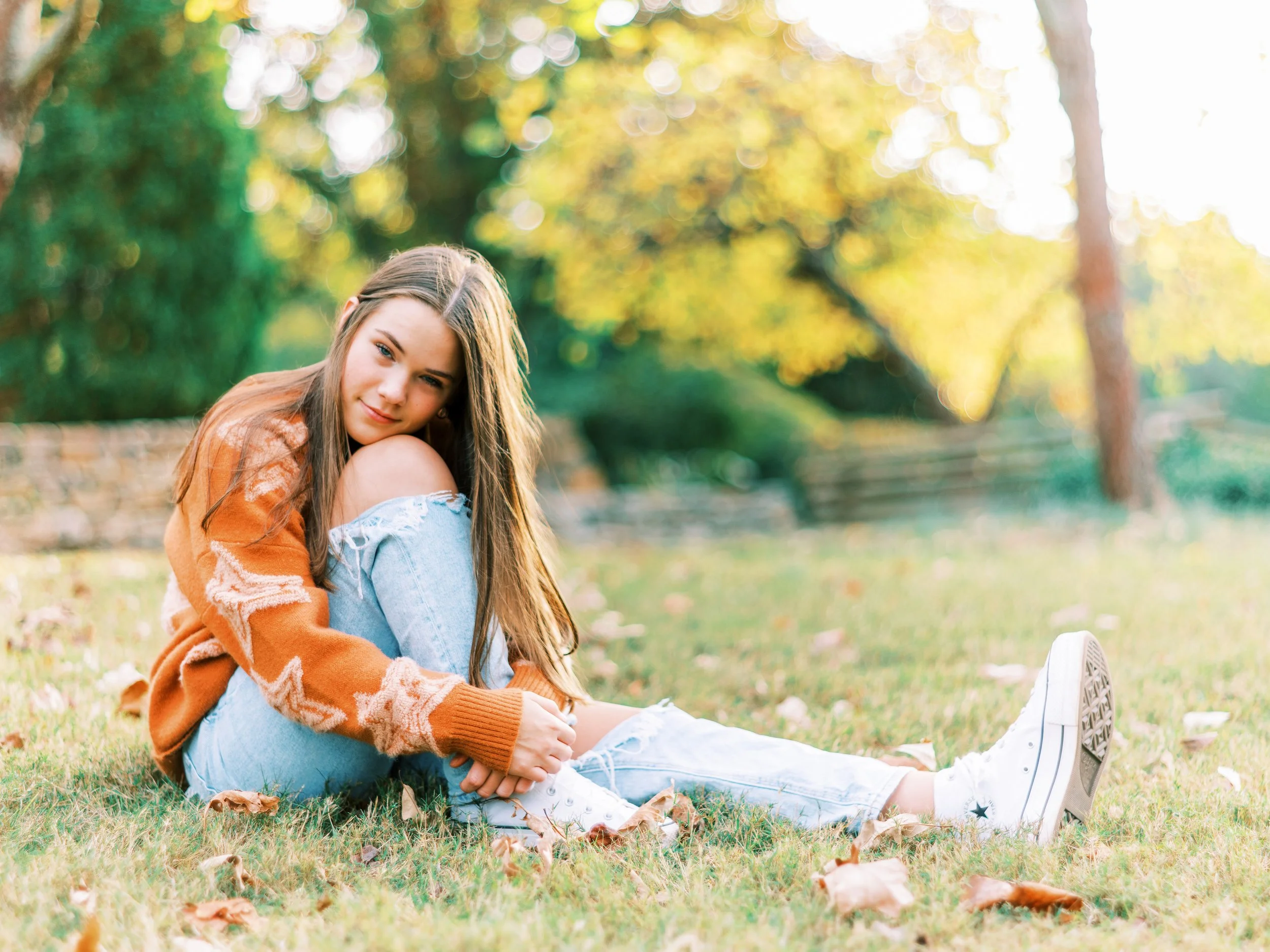 Senior portrait of Hannah sitting on the grass in an orange cardigan over a denim off-shoulder top at Kennesaw Mountain Battlefield Park in Kennesaw, Georgia