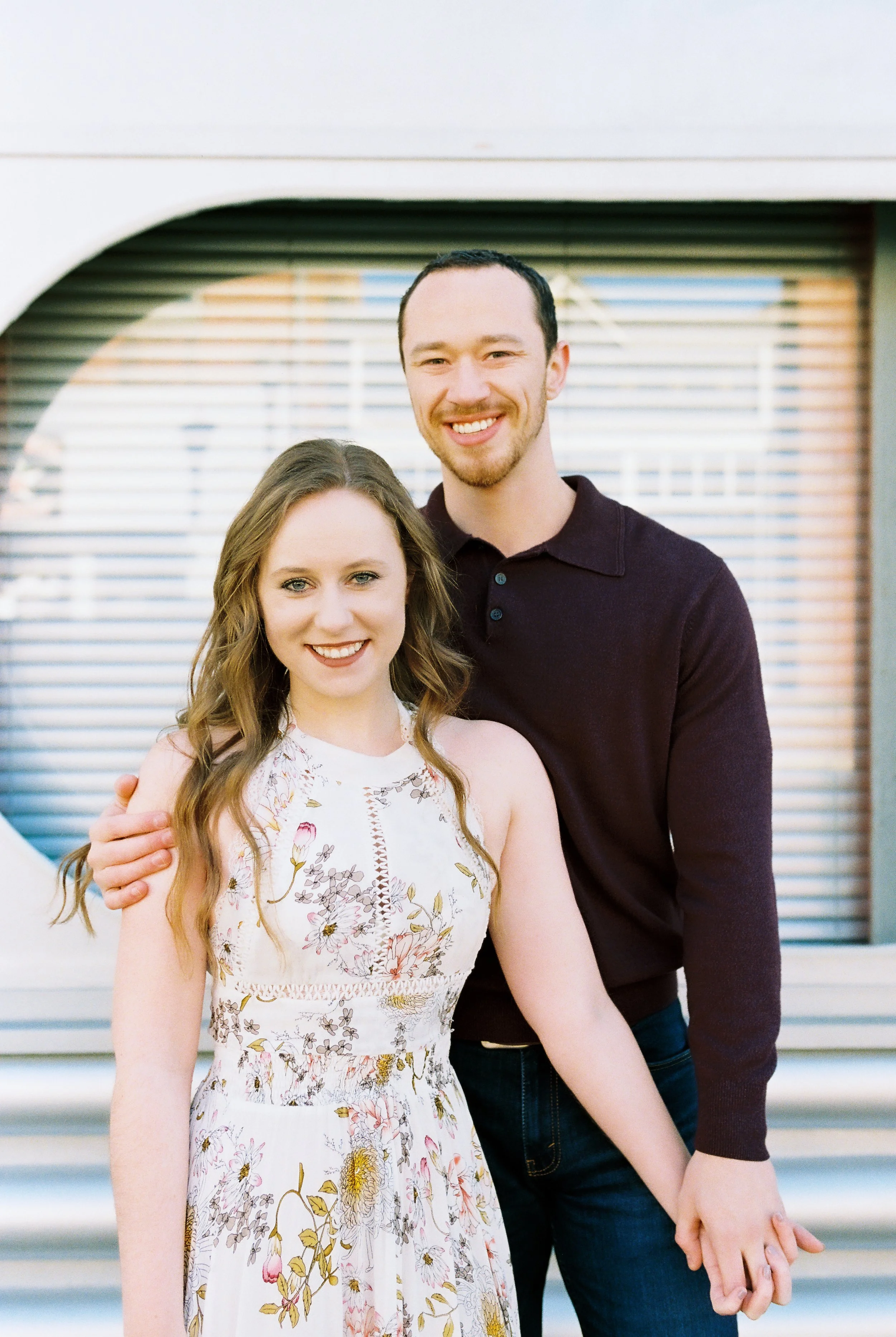 Conner and Maddie smile at the camera in front of a storefront in downtown Dallas, Georgia during their engagement session.
