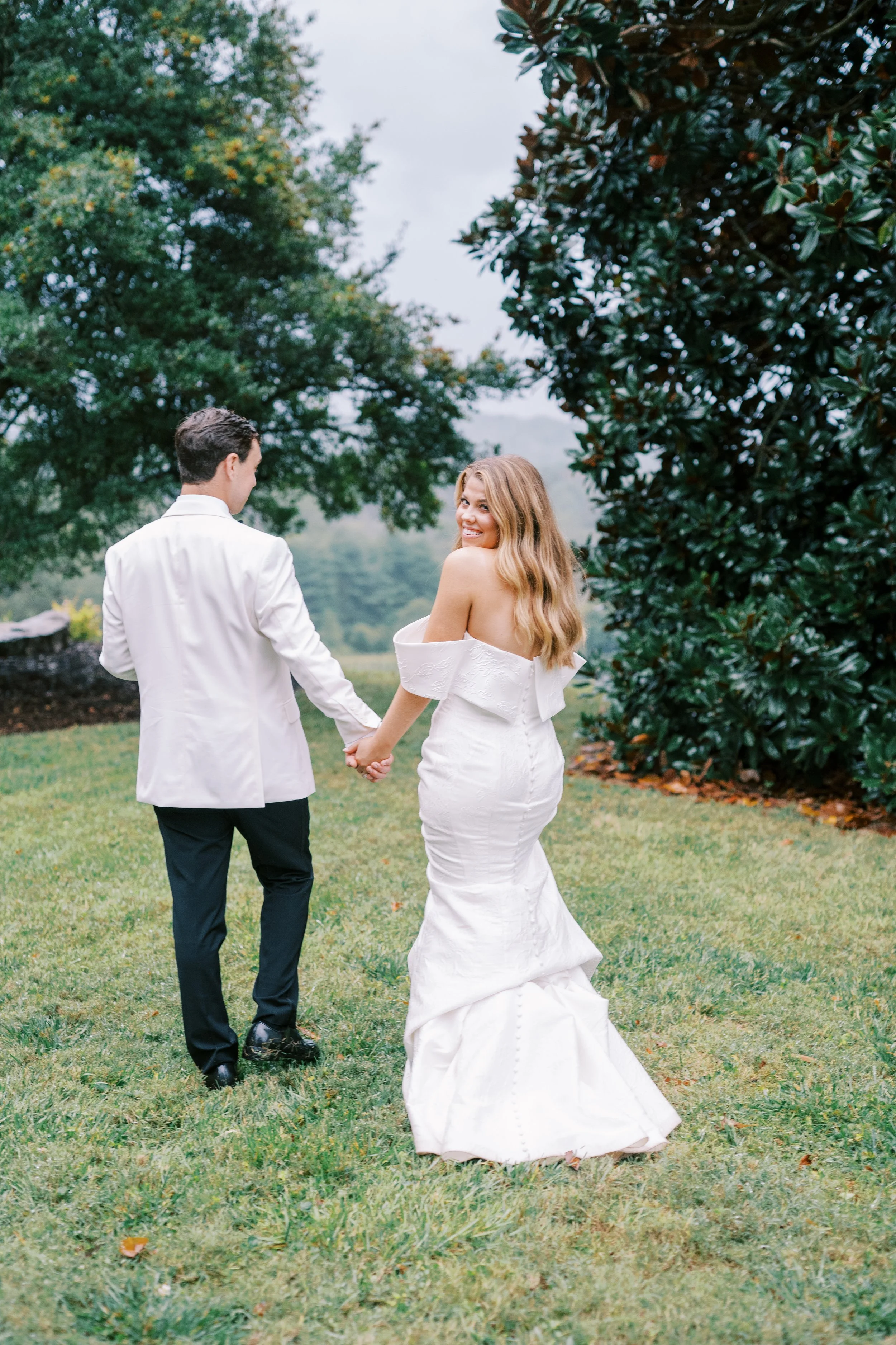 Bride and groom walking hand in hand outdoors, viewed from behind
