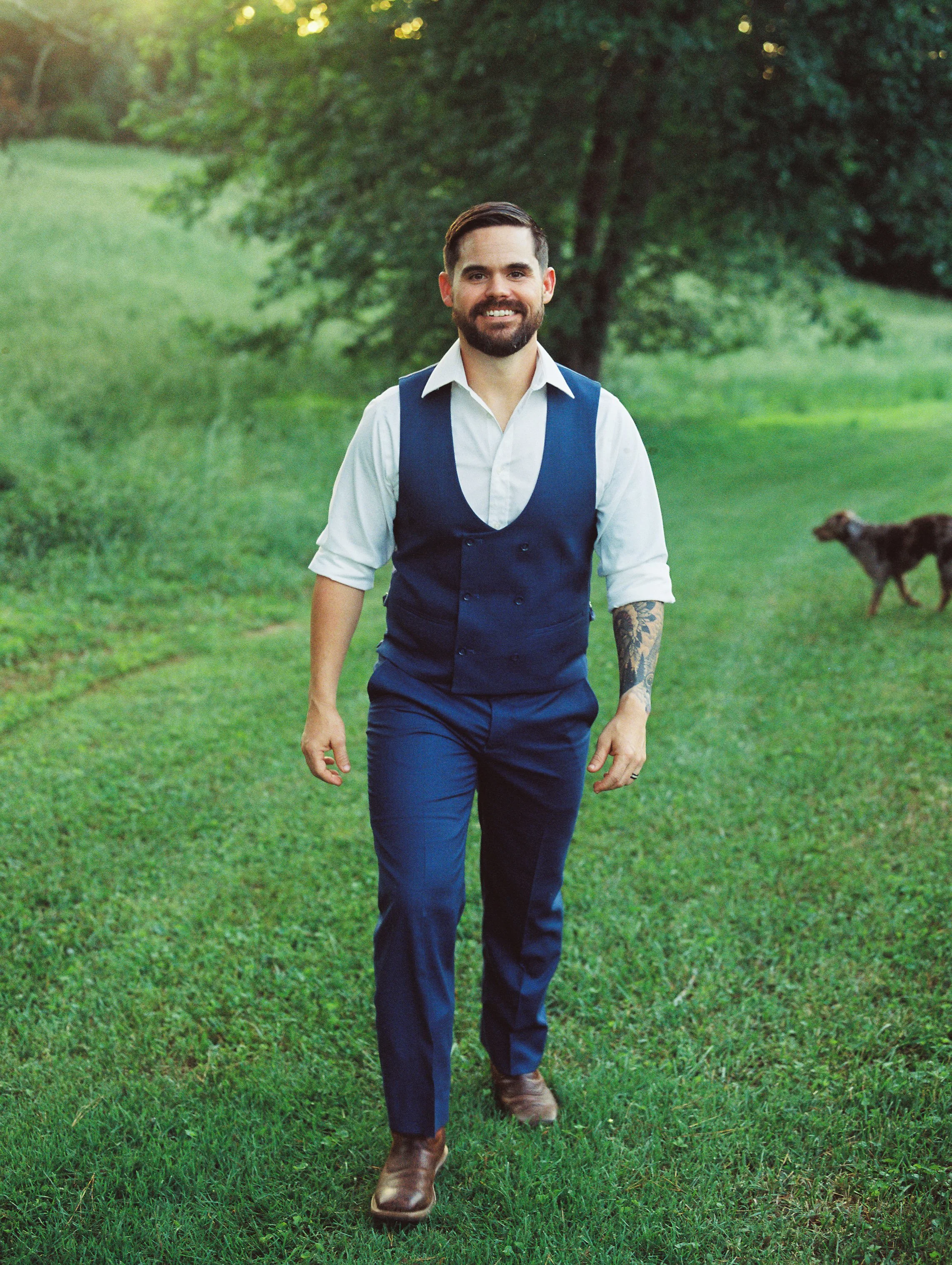 Groom walking across the lawn with the couple's dog Dakota following behind