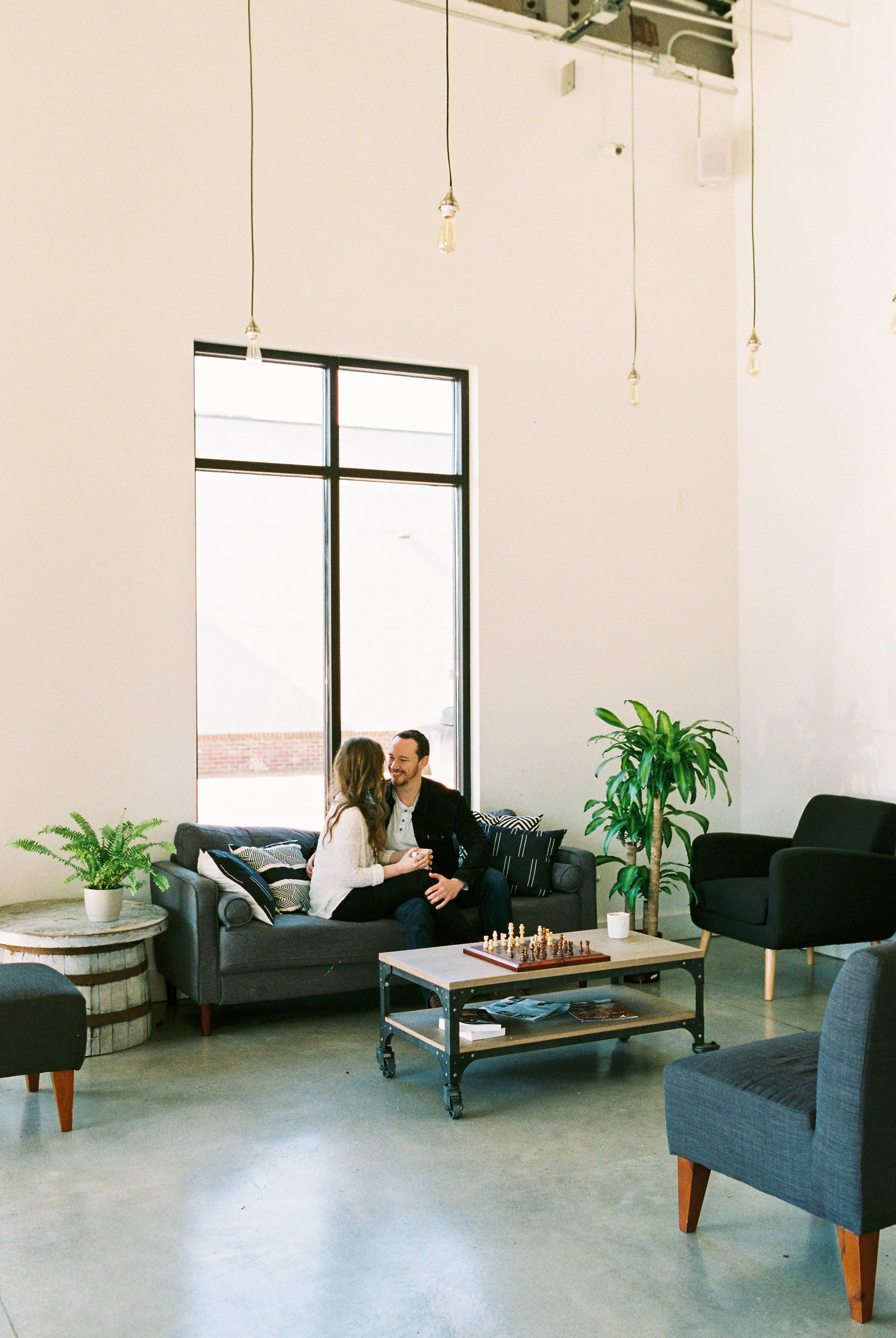 A wide view of Conner and Maddie sitting together in the lounge area of a Dallas, Georgia coffee shop, chess board on the table.