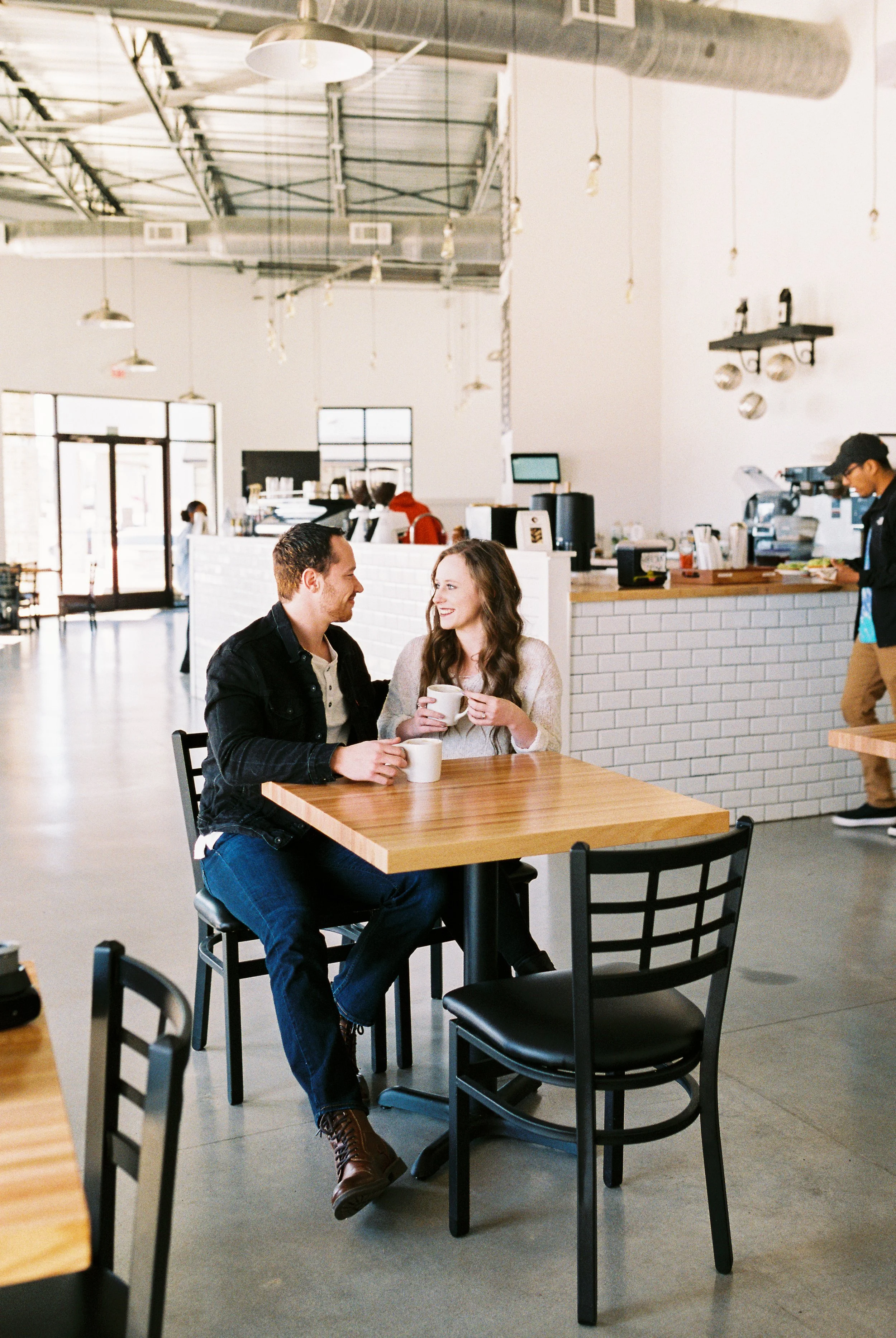A wide view of Conner and Maddie talking over coffee near the counter of a Dallas, Georgia coffee shop.