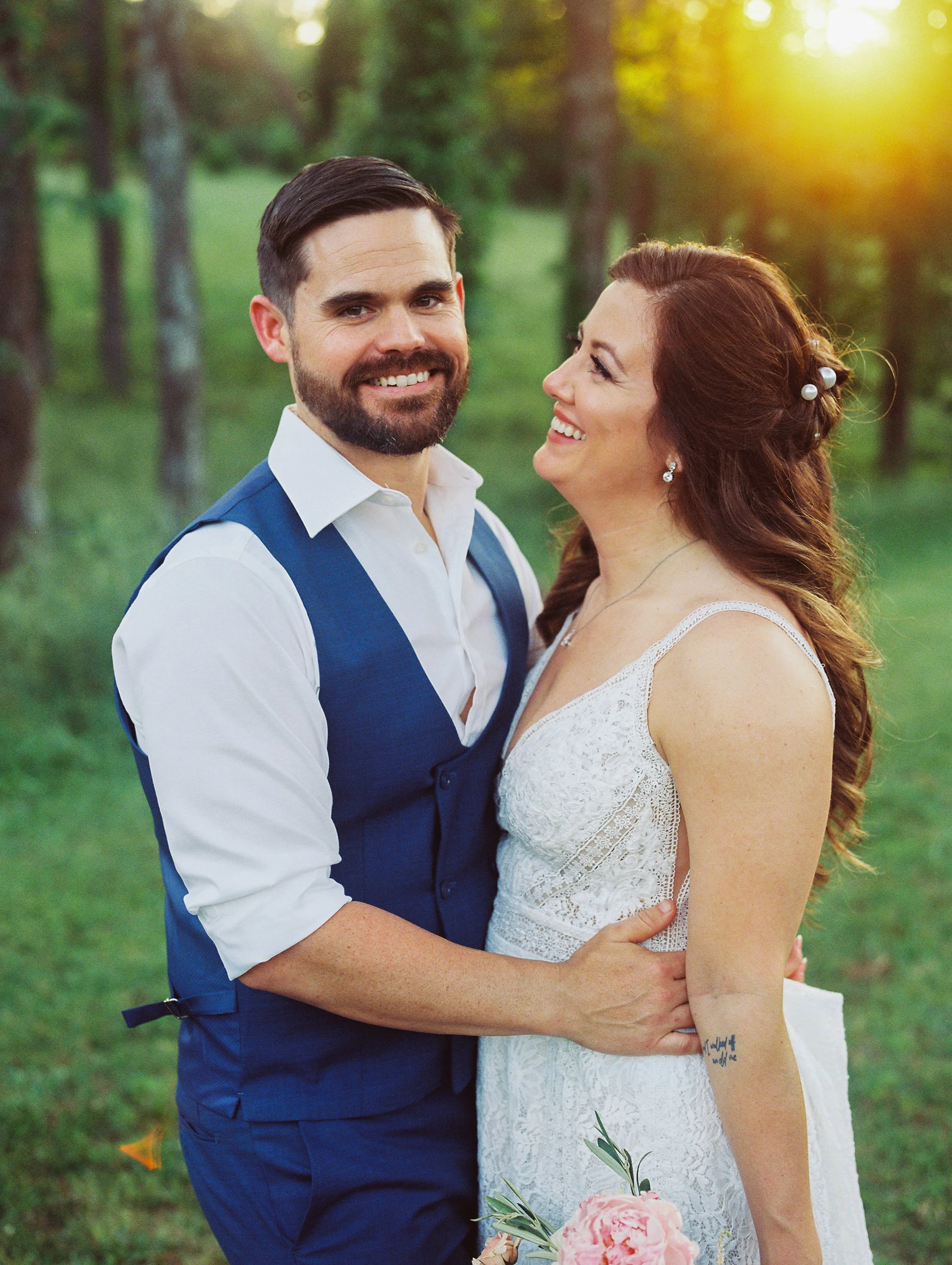 Bride and groom smiling closely together in the woods with warm evening light behind them
