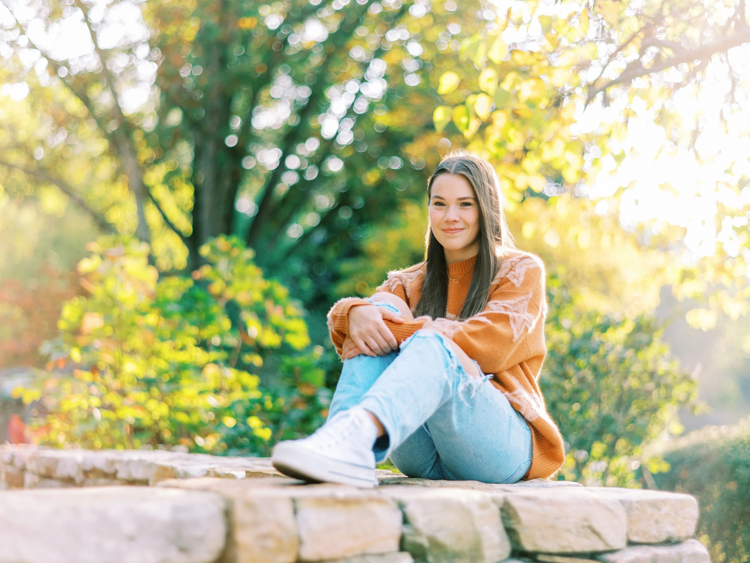 Senior portrait of Hannah relaxing on a stone wall in an orange sweater at Kennesaw Mountain Battlefield Park in Kennesaw, Georgia
