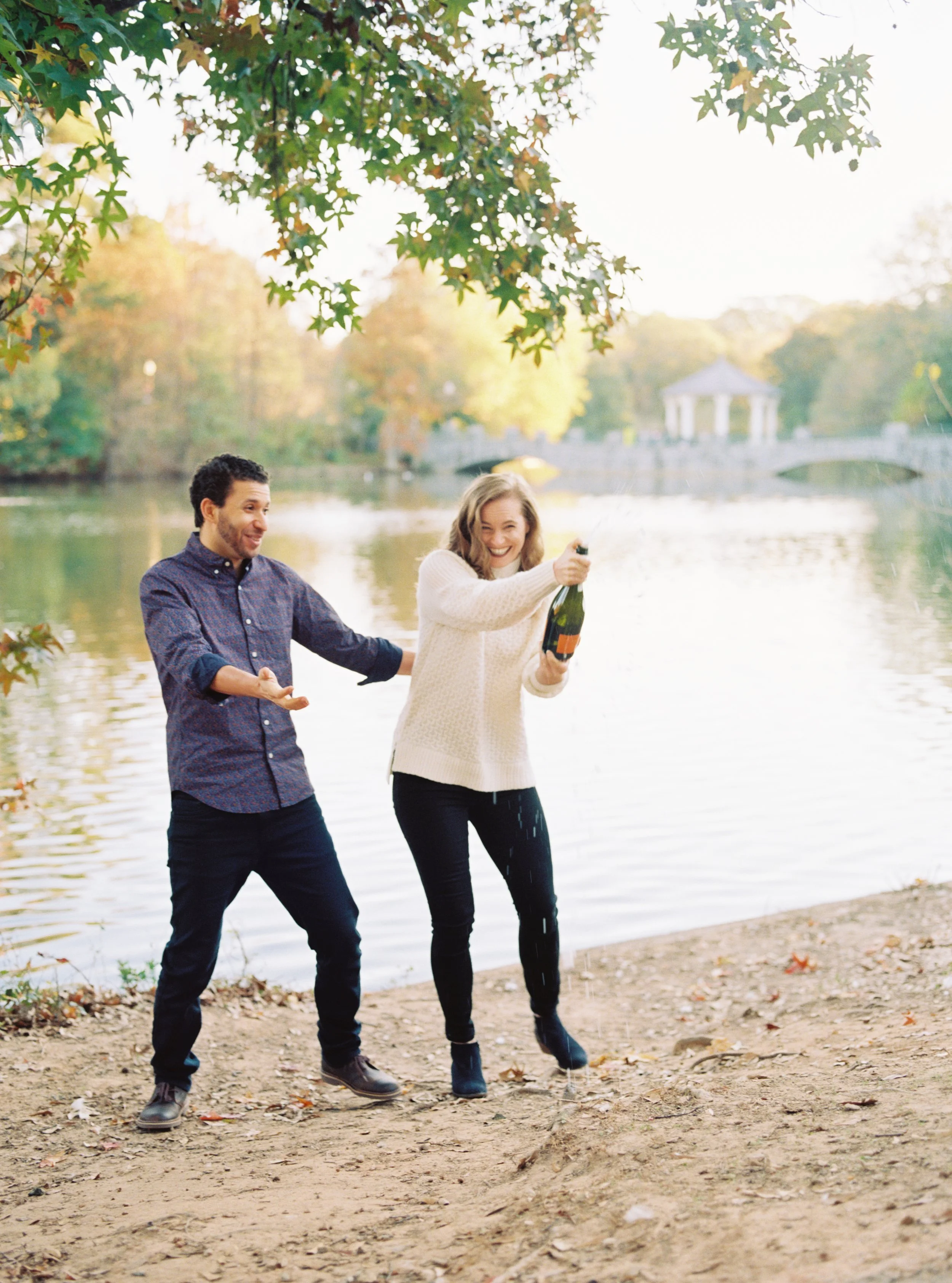 Couple laughing as she pops a champagne bottle by the lakeshore
