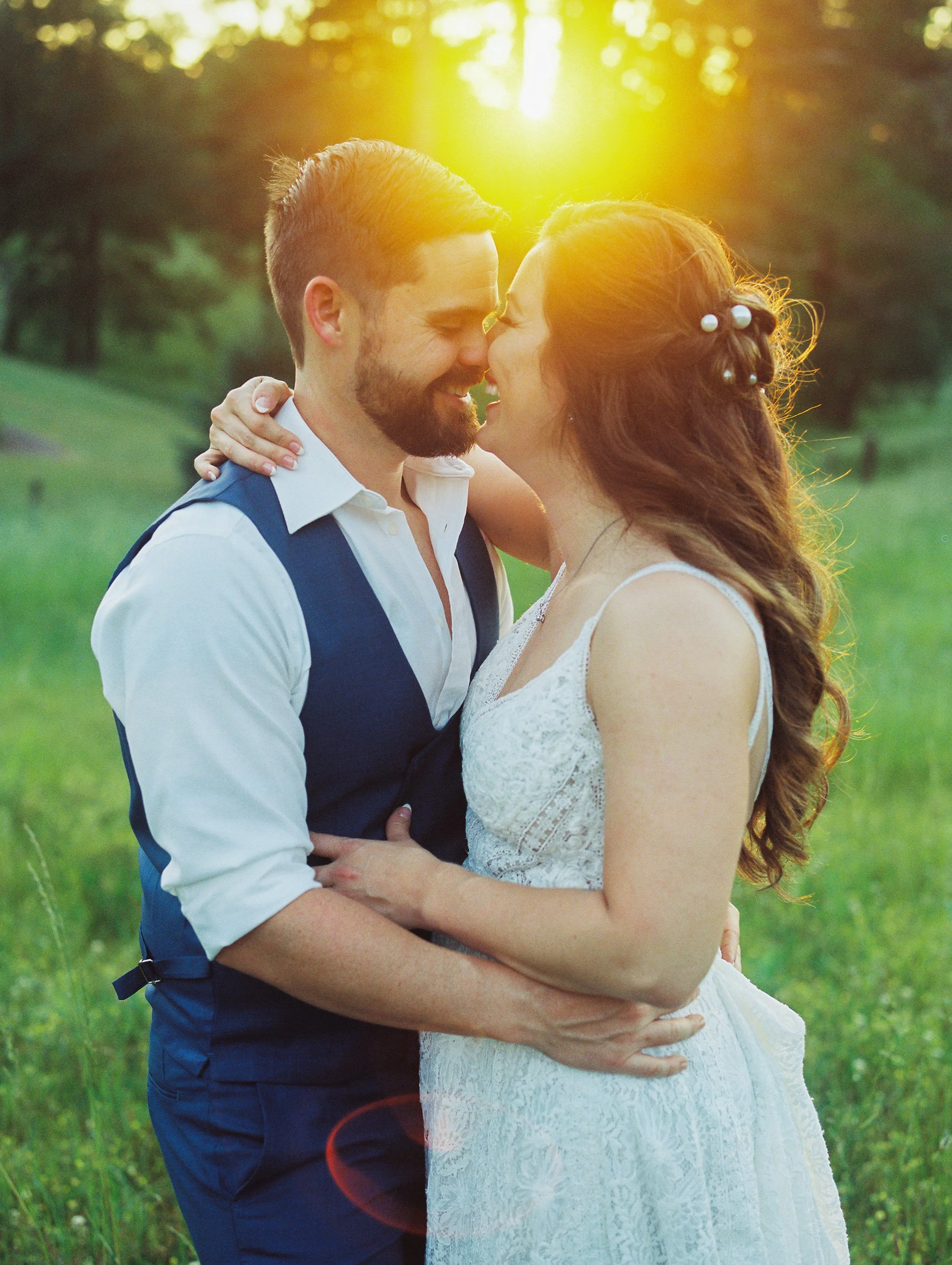 Bride and groom about to kiss with the sun flaring behind them in a grassy field