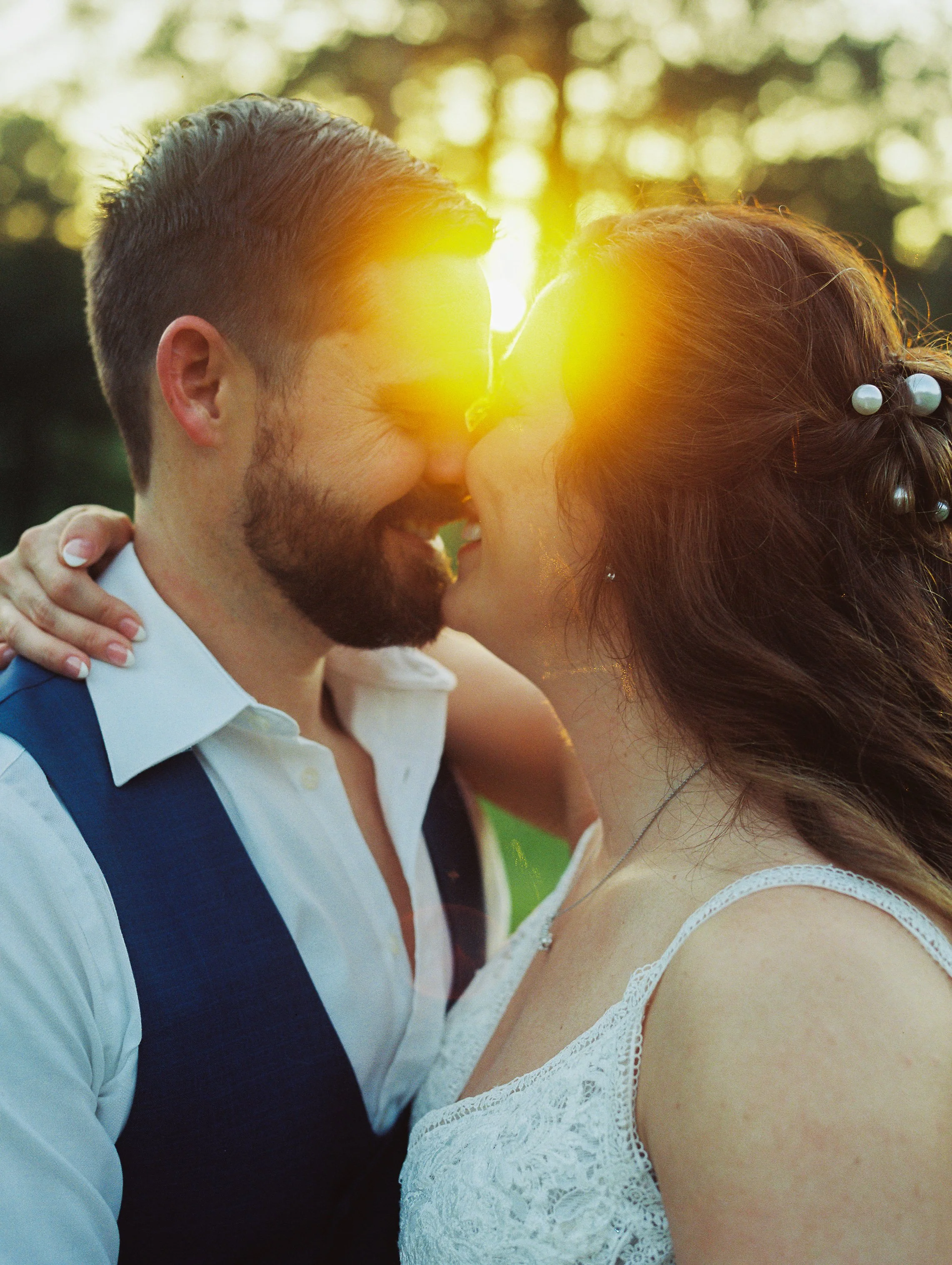 Close-up of bride and groom nose to nose with dramatic sun flare between them