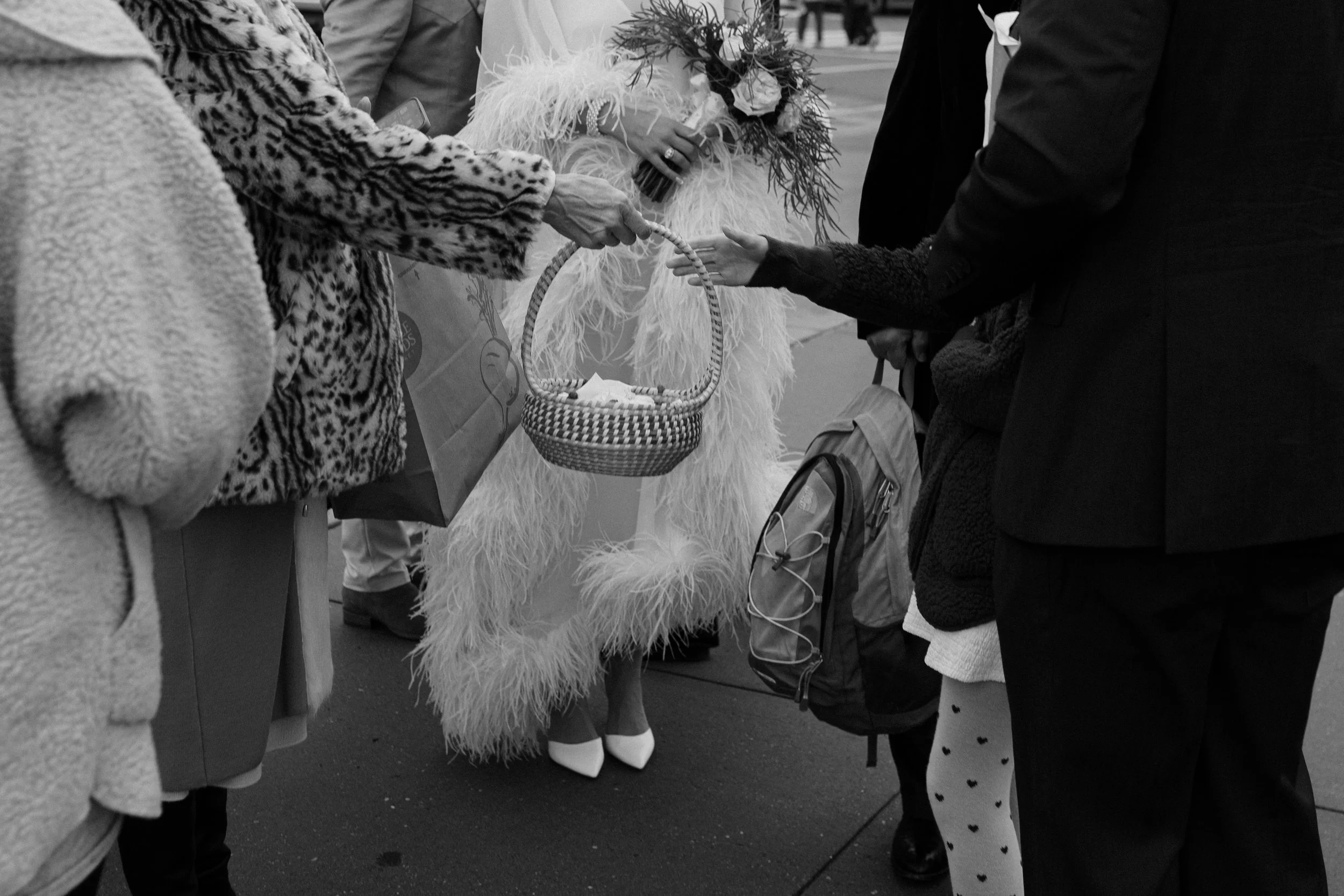 Black and white detail photo of the bride adjusting her feathered dress on the street