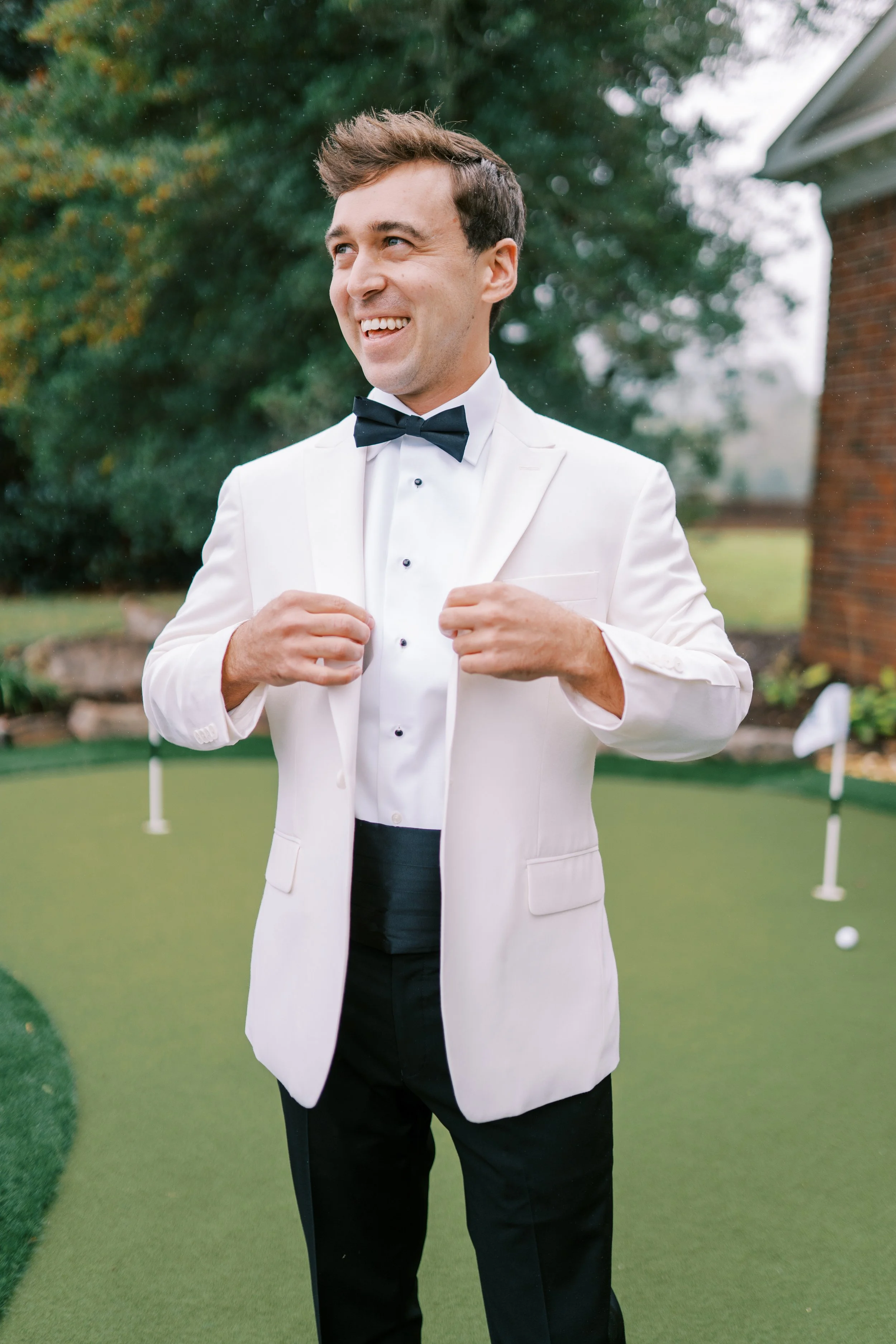 Groom buttoning his white tuxedo jacket before the ceremony