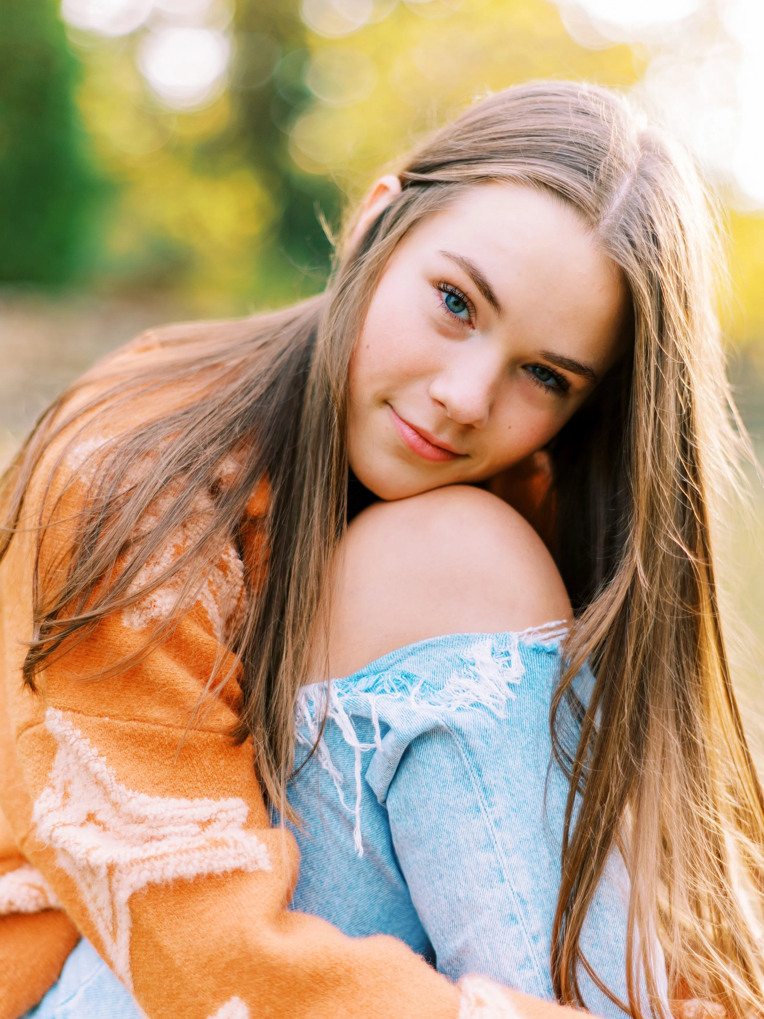 Close-up senior portrait of Hannah wearing an orange cardigan over a denim off-shoulder top at Kennesaw Mountain Battlefield Park in Kennesaw, Georgia