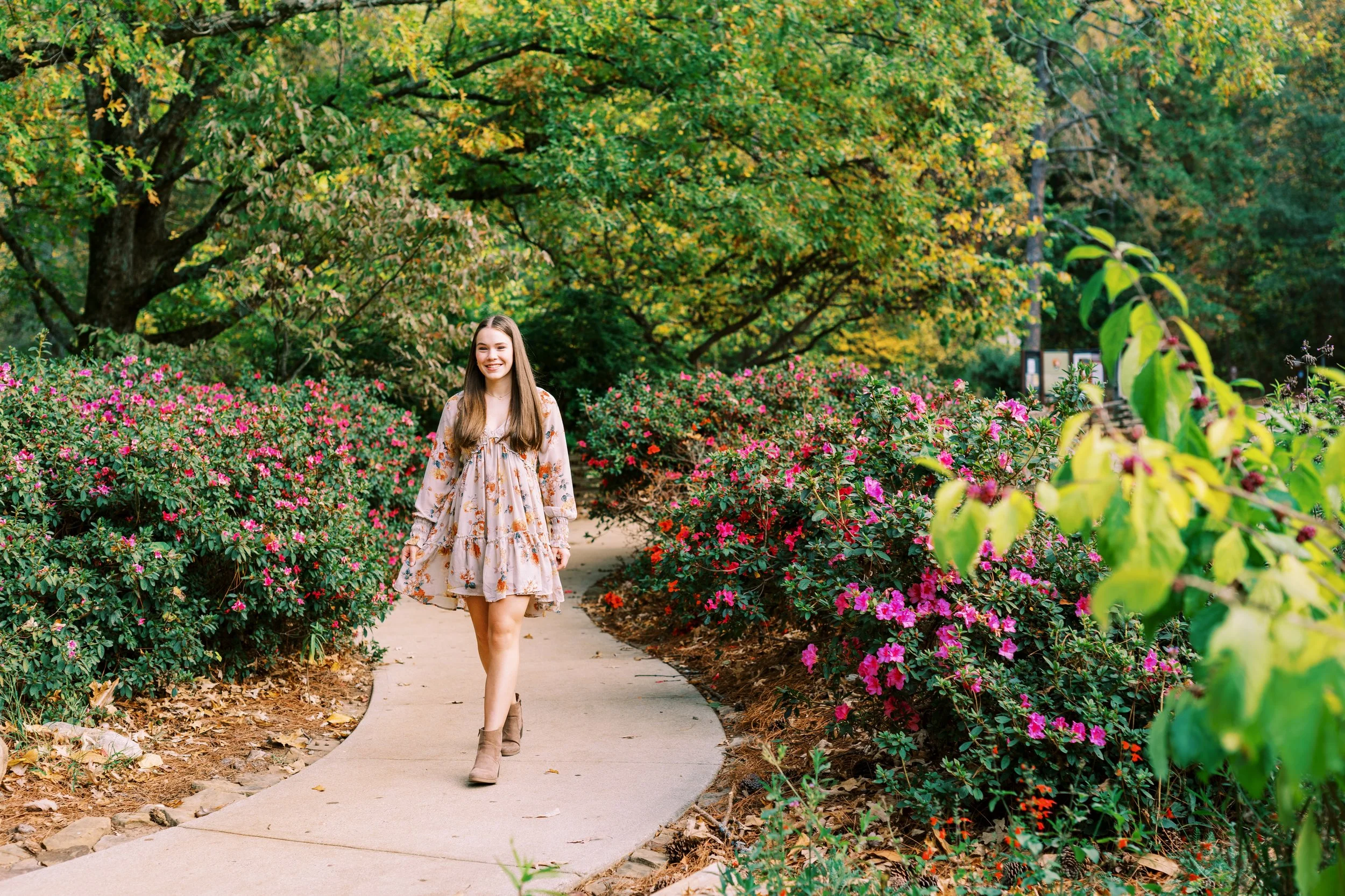Senior portrait of Hannah walking down a garden path in a floral dress at Kennesaw Mountain Battlefield Park in Kennesaw, Georgia