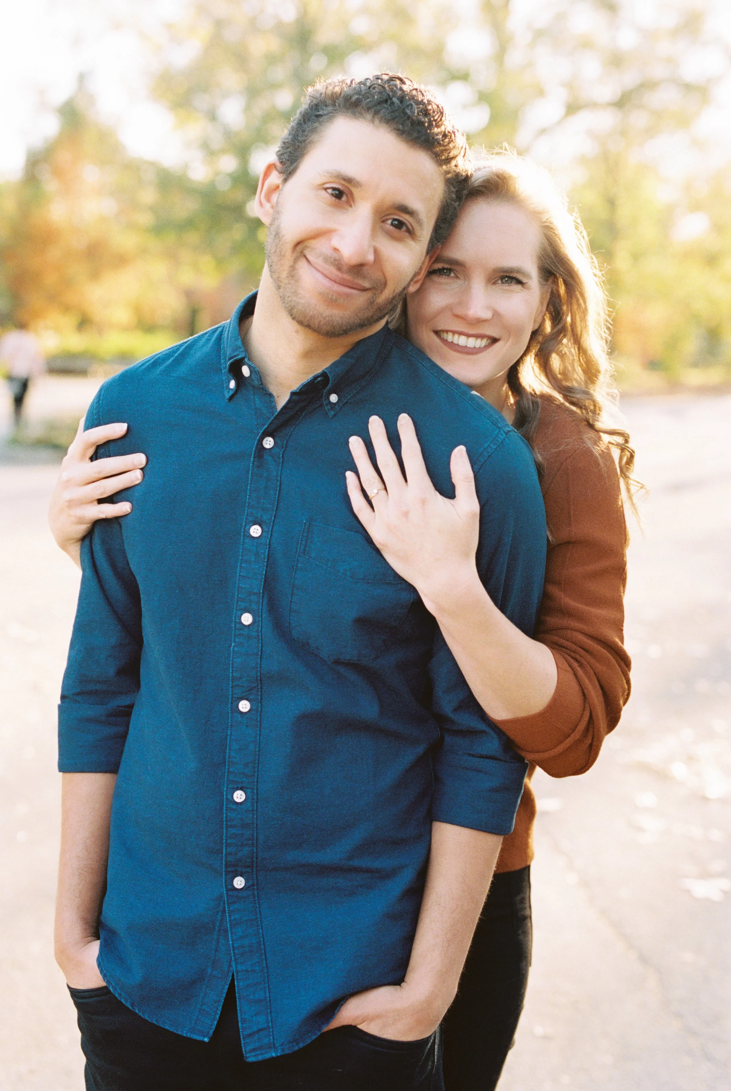 Bride-to-be hugging her fiance from behind while playfully showing off her engagement ring