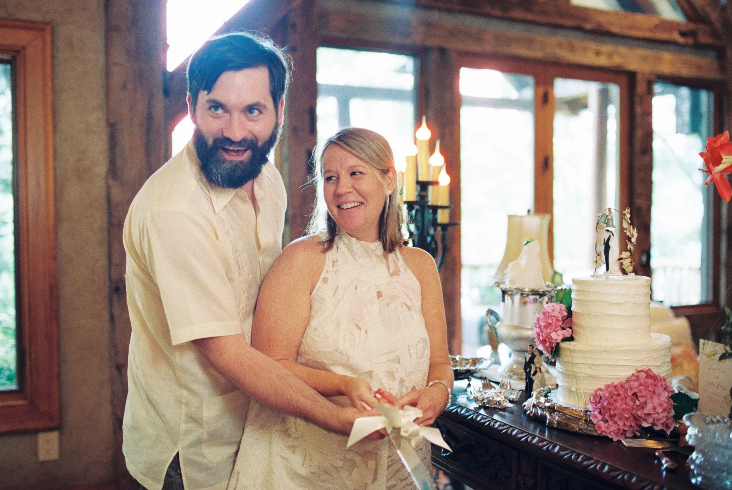 Bride and groom smiling together indoors with their wedding cake displayed on the table behind them