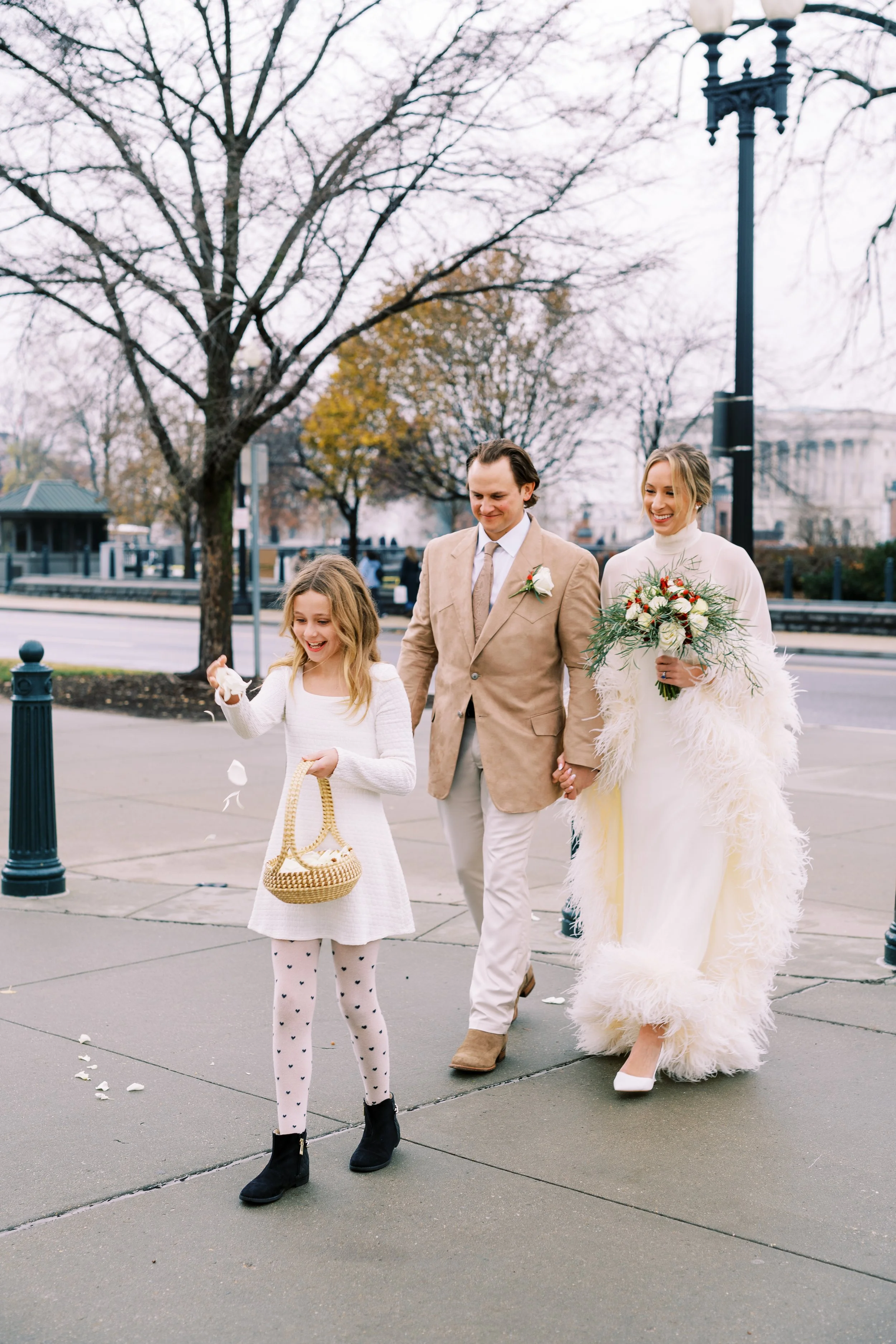 Bride and groom walking with a flower girl on a Washington DC street lined with bare trees