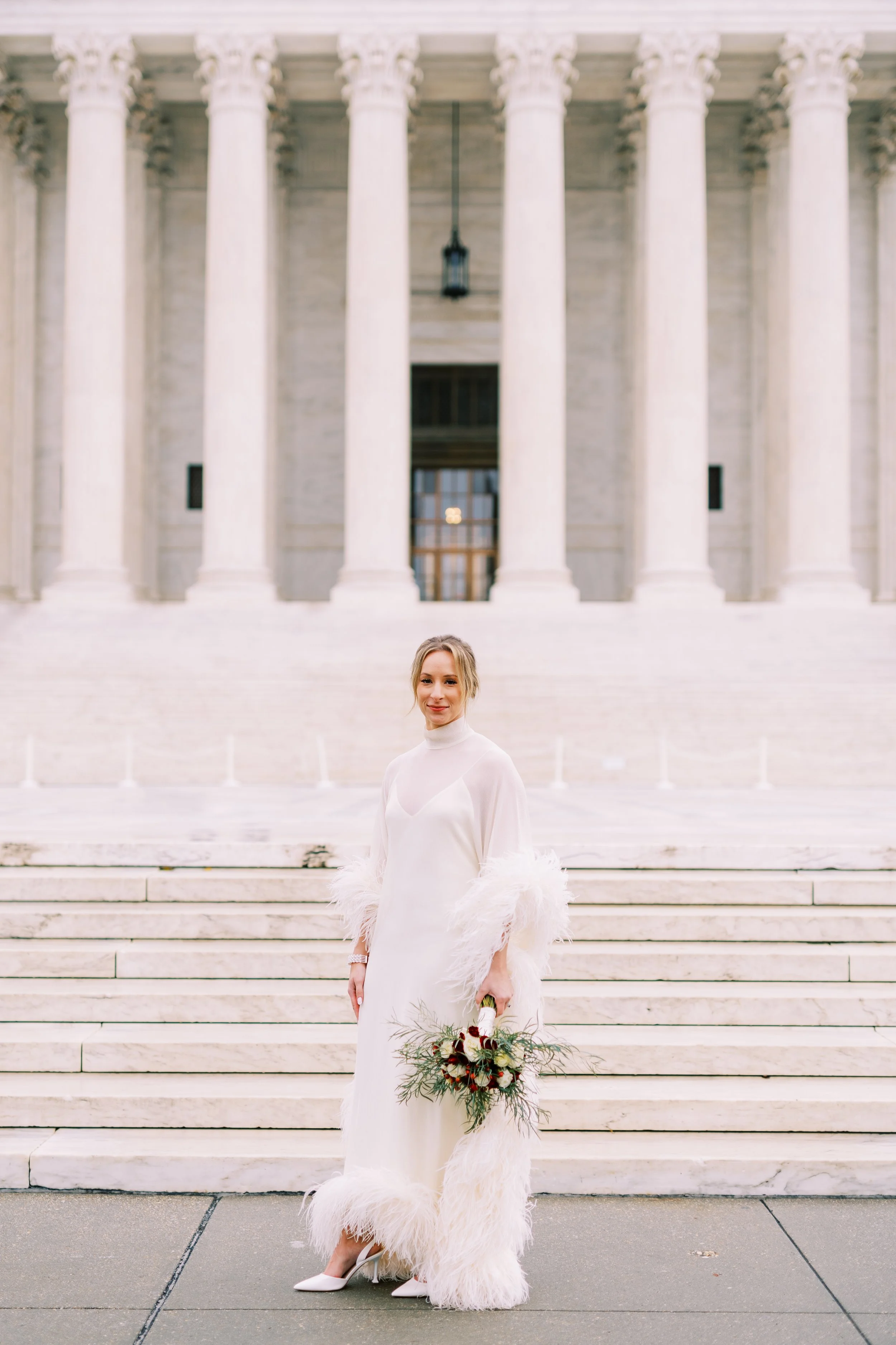 Bride standing solo on the steps of a grand columned building holding her bouquet