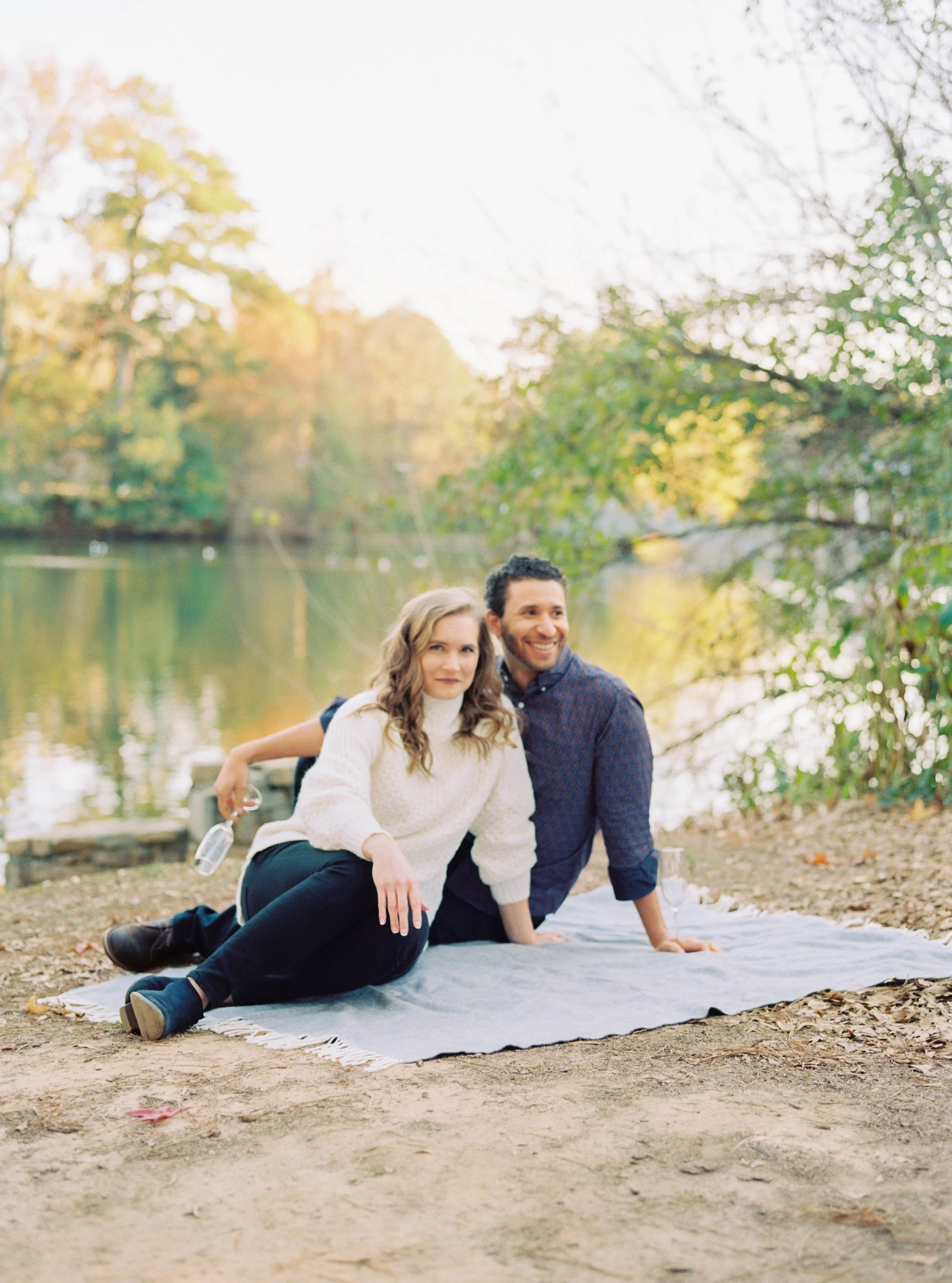 Couple sitting together on a picnic blanket by the lakeshore, smiling