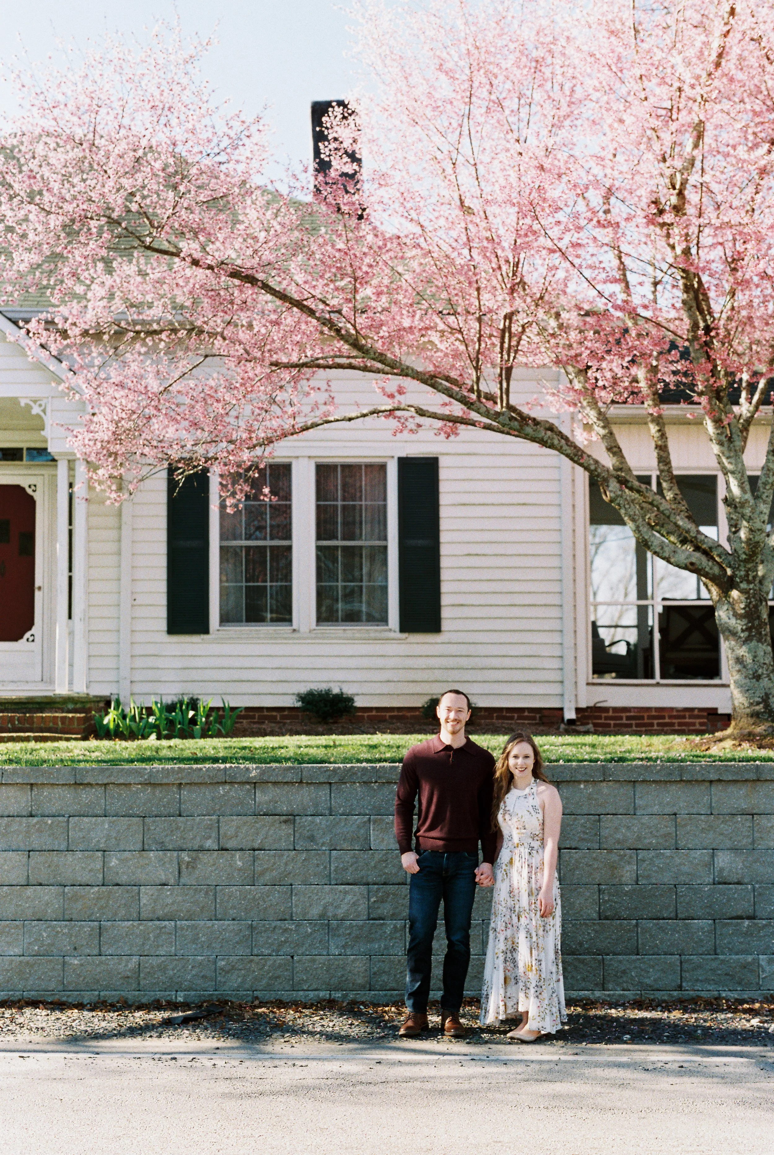 Conner and Maddie stand hand in hand in front of a house with a blooming pink cherry tree in Dallas, Georgia.