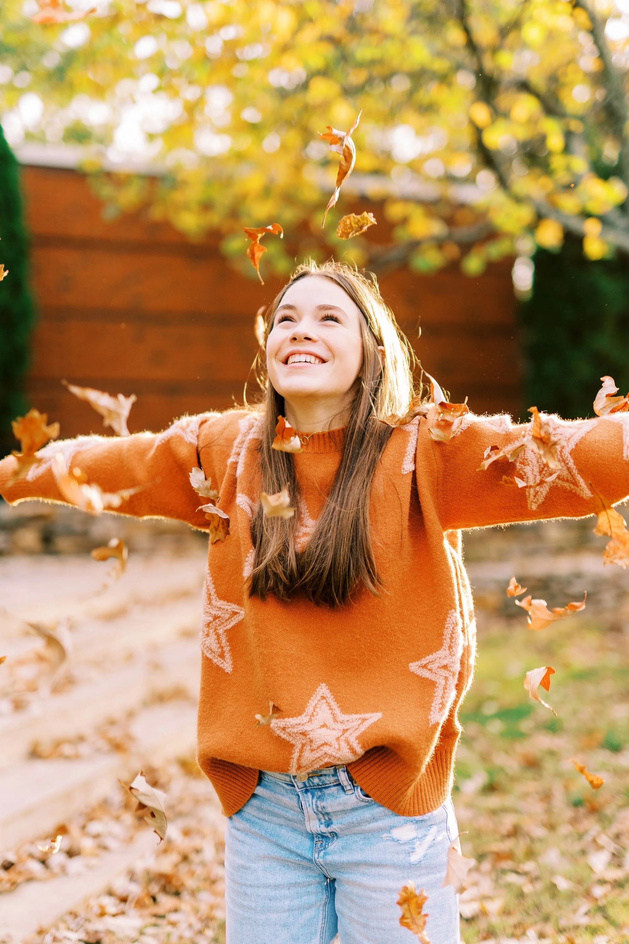Senior portrait of Hannah laughing and throwing fall leaves in an orange sweater at Kennesaw Mountain Battlefield Park in Kennesaw, Georgia