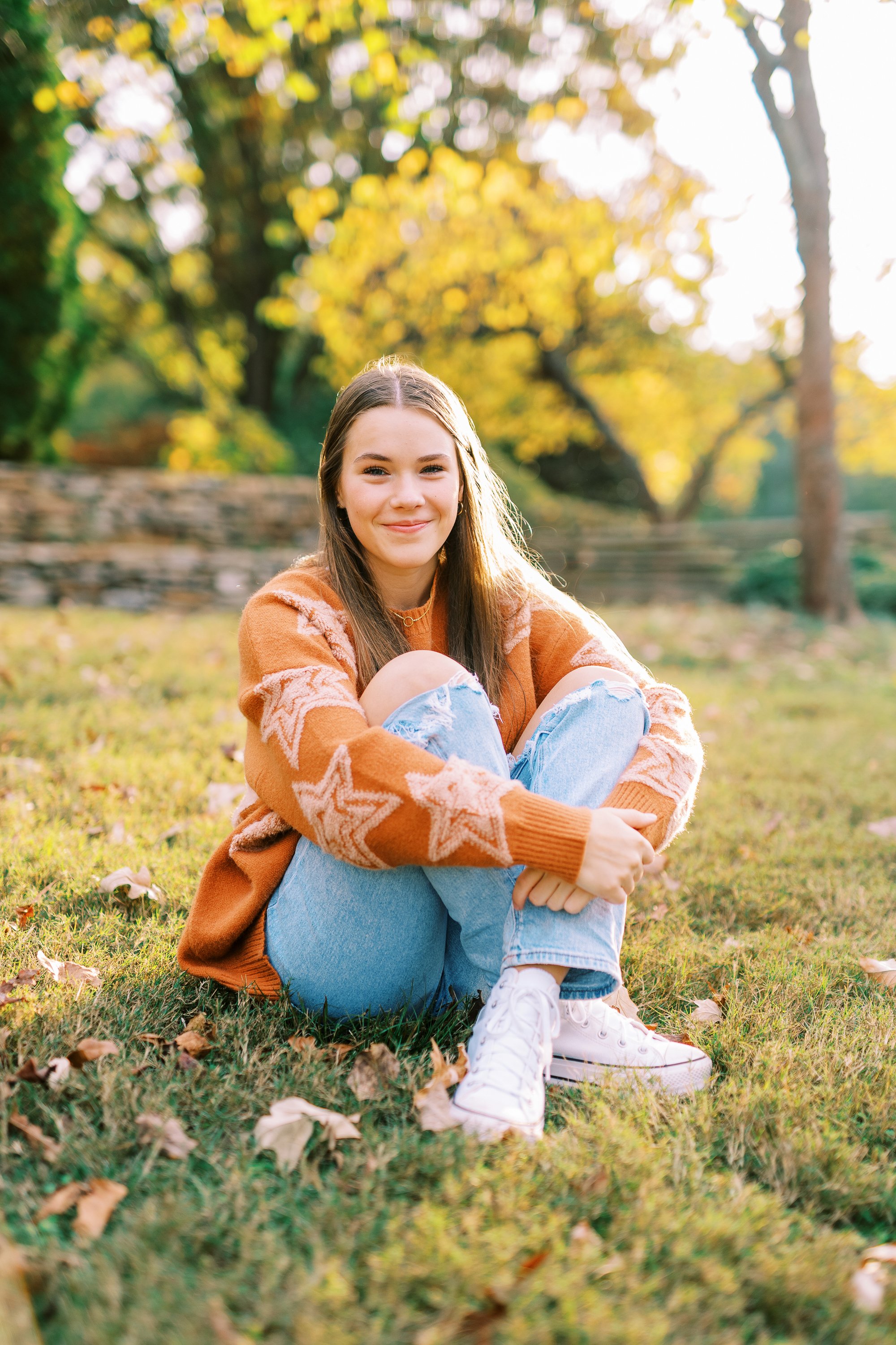 Senior portrait of Hannah crouching in the grass hugging her knees in an orange sweater at Kennesaw Mountain Battlefield Park in Kennesaw, Georgia