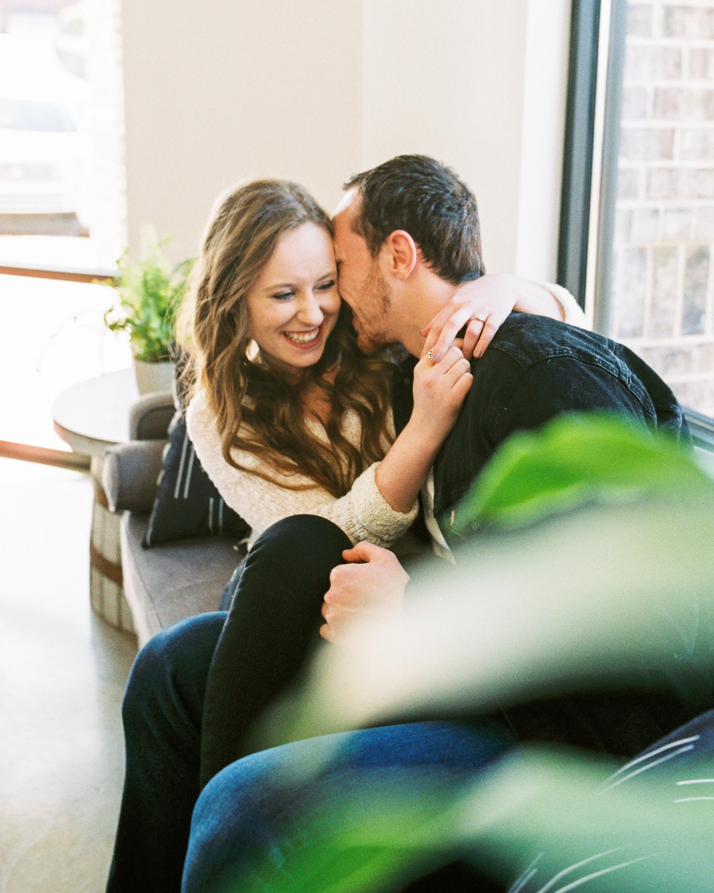Conner kisses Maddie's hair as she laughs on a couch in a Dallas, Georgia coffee shop.