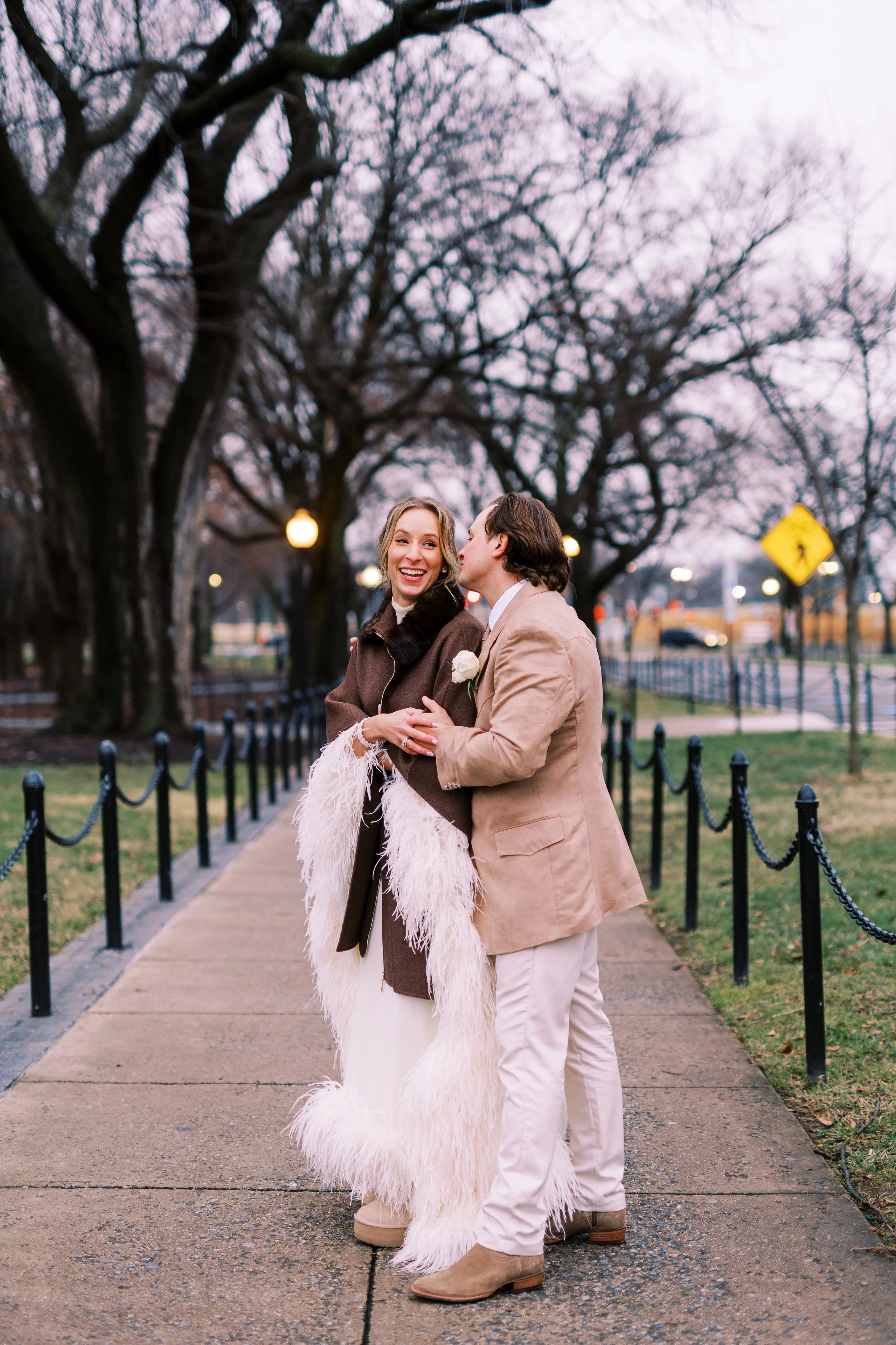 Bride and groom embracing on a tree-lined path at dusk
