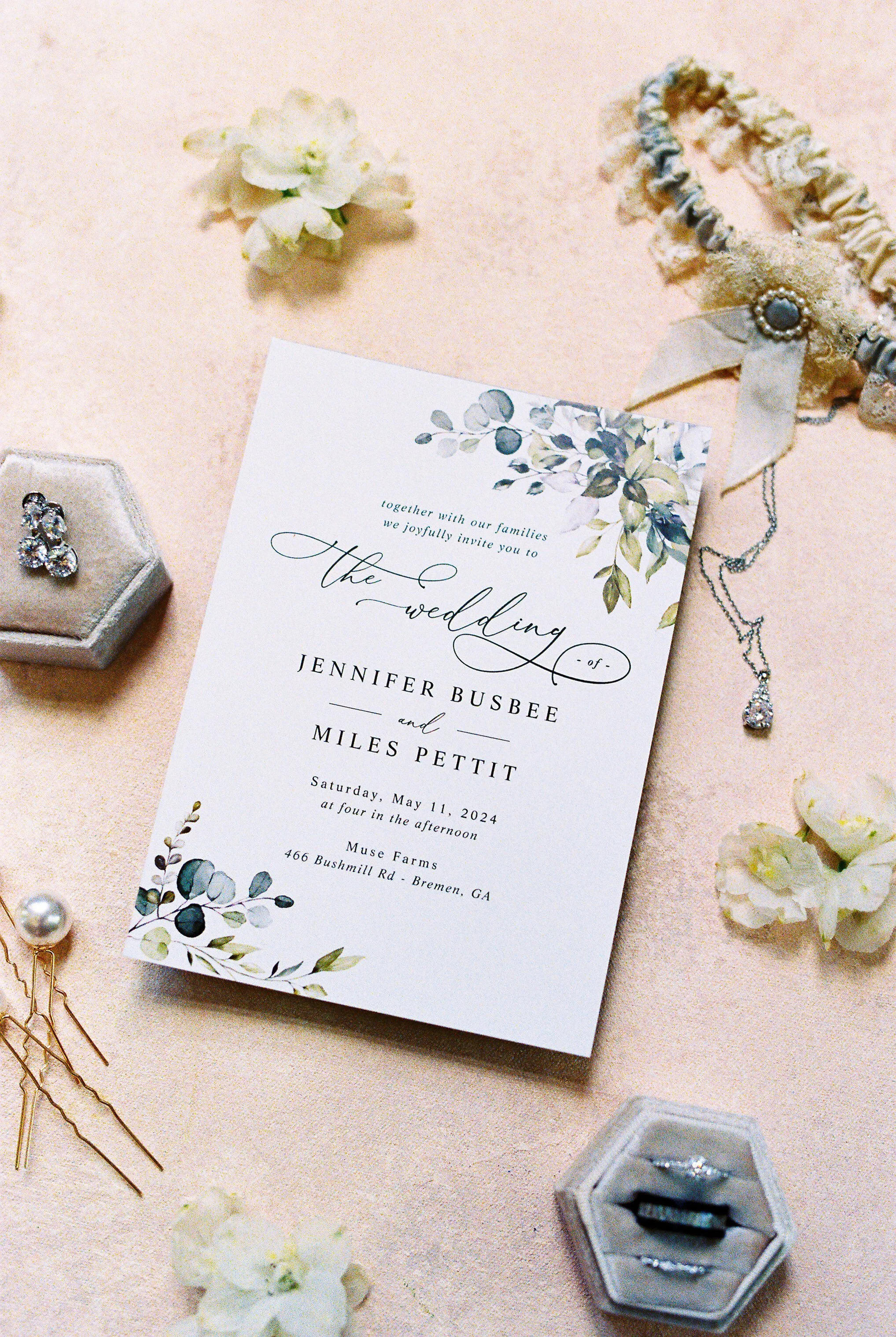 Wedding invitation flat lay with jewelry and hair pins for Jenni and Miles's Muse Farms wedding in Bremen, Georgia