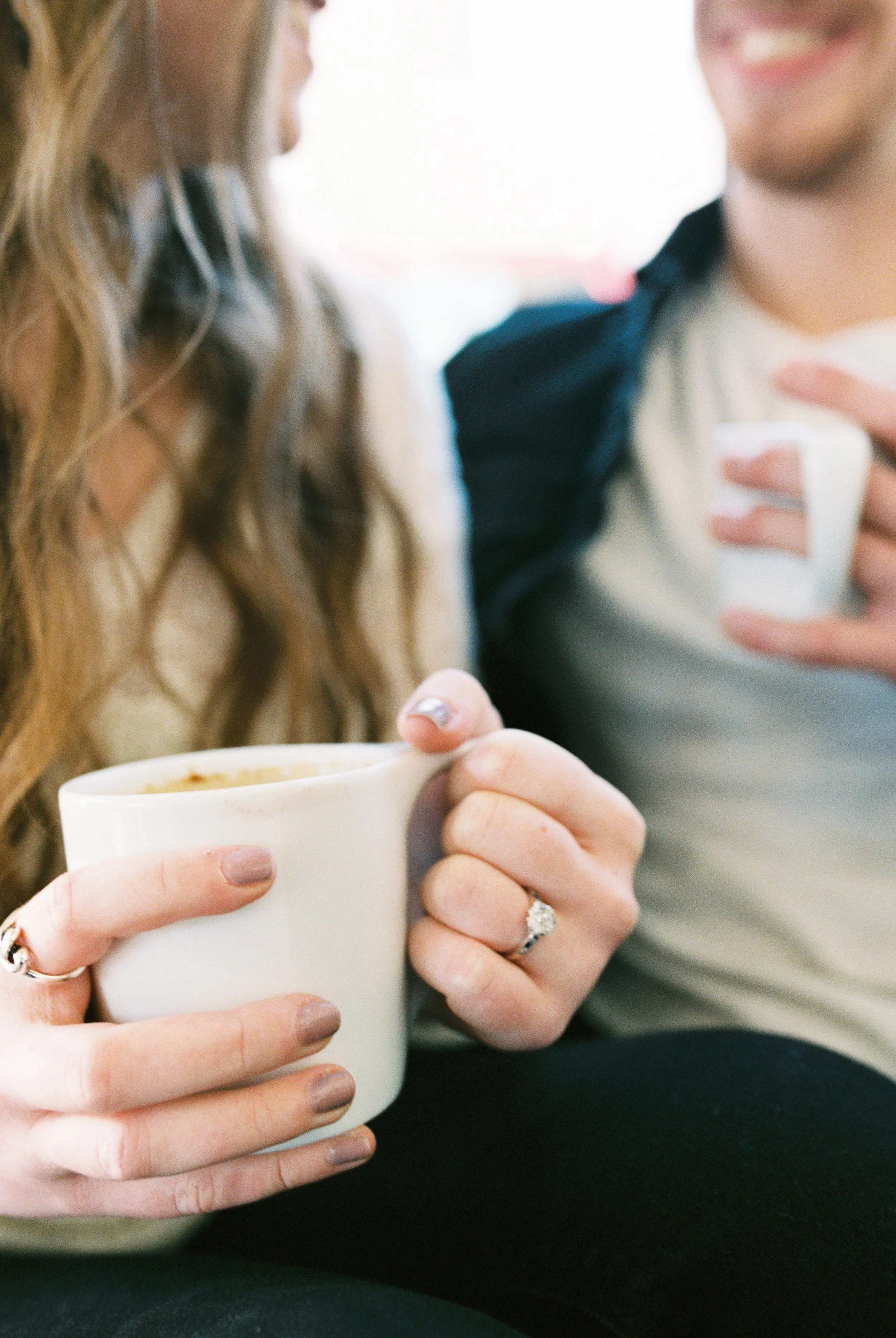 A detail shot of Conner and Maddie holding coffee mugs, her engagement ring visible, in a Dallas, Georgia coffee shop.