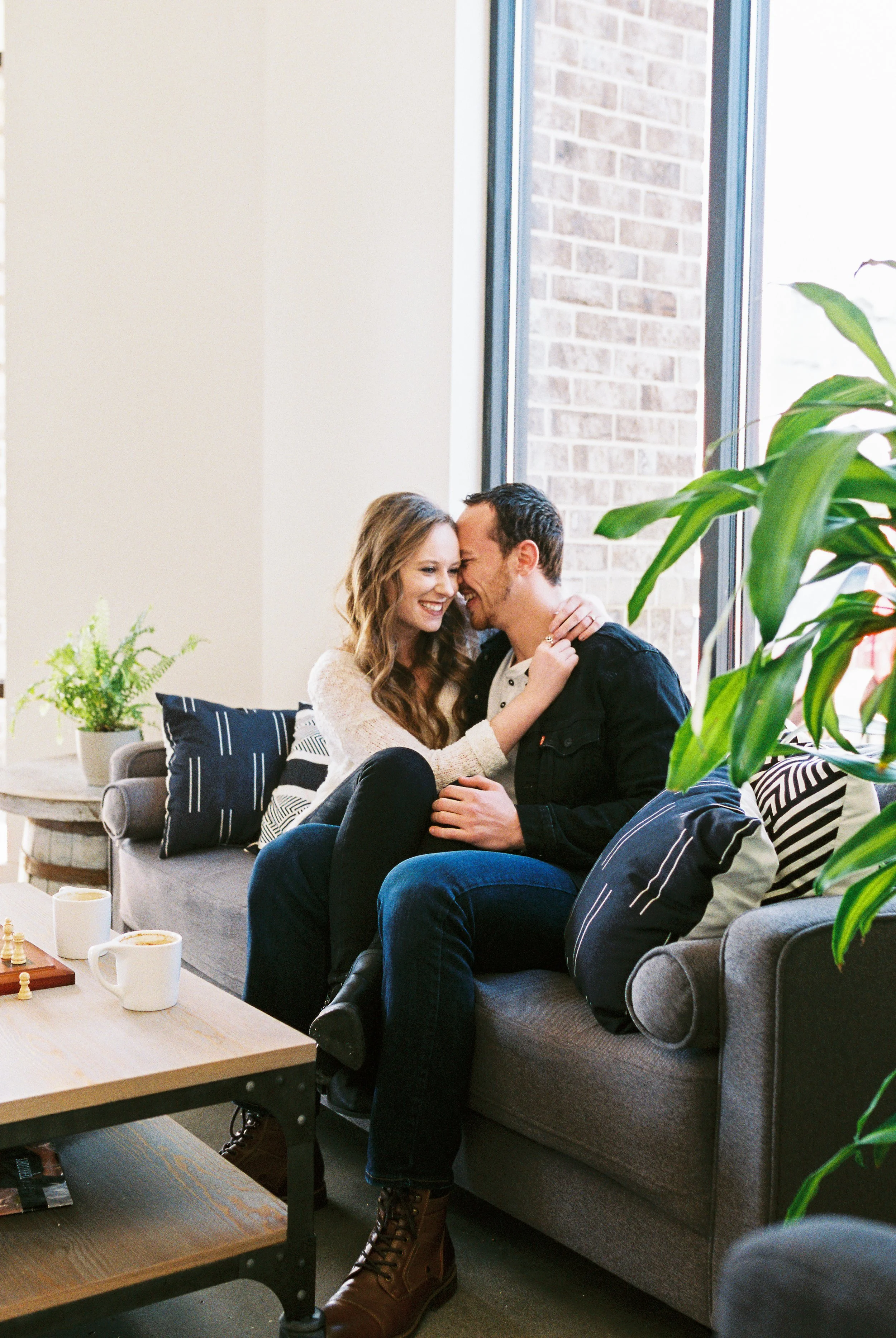 Conner and Maddie laugh together close on a couch by a brick wall window in a Dallas, Georgia coffee shop.