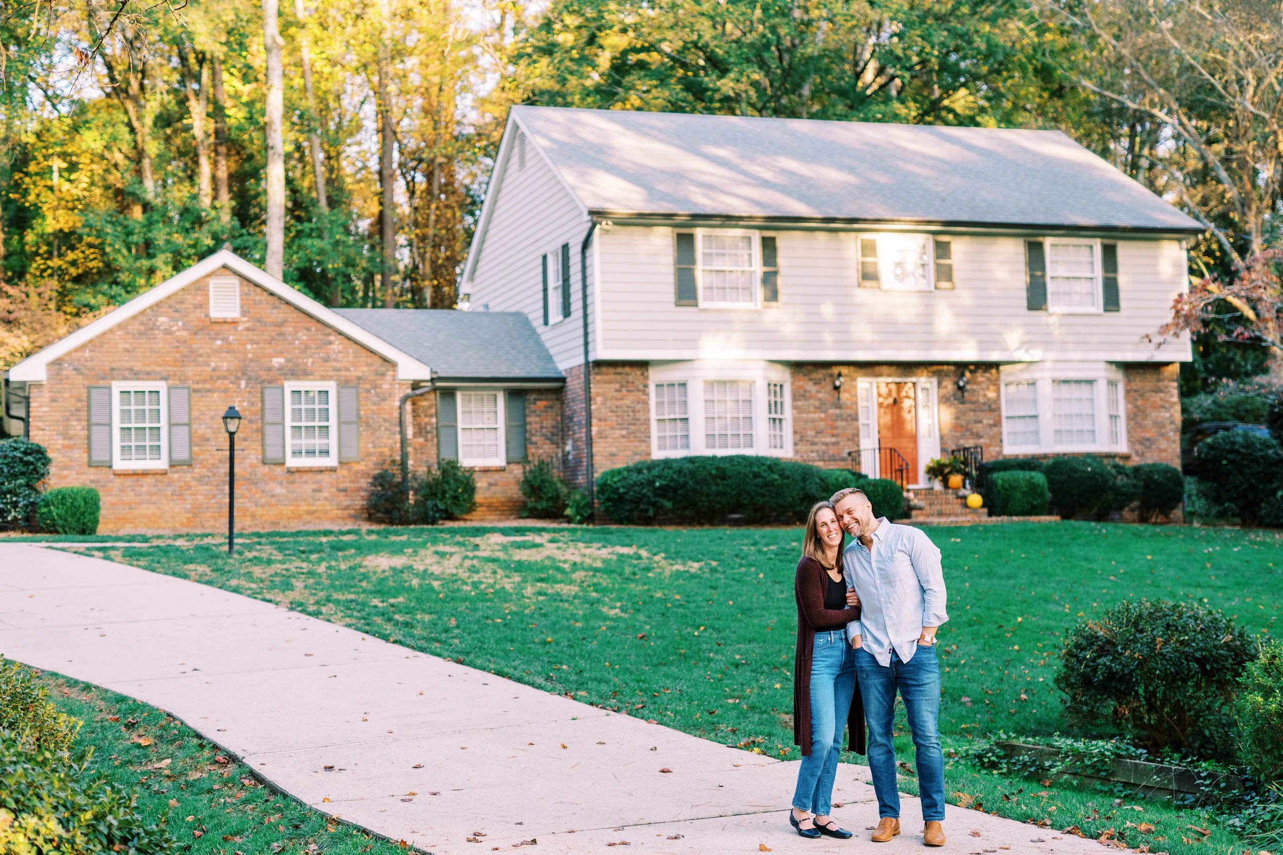 Holly and Chris embracing on the front lawn of their brick colonial home in Dunwoody, Georgia